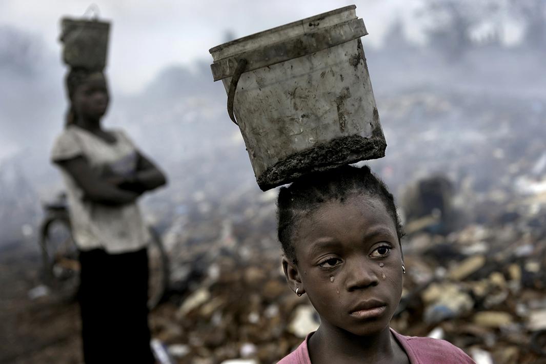 In an e-waste dump that kills nearly everything that it touches, Fati, 8, works with other children searching through hazardous waste in hopes of finding whatever she can to exchange for pennies in order to survive. While balancing a bucket on her head with the little metal she has found, tears stream down her face as the result of the pain that comes with the malaria she contracted some years ago. This is work she must do to survive. 