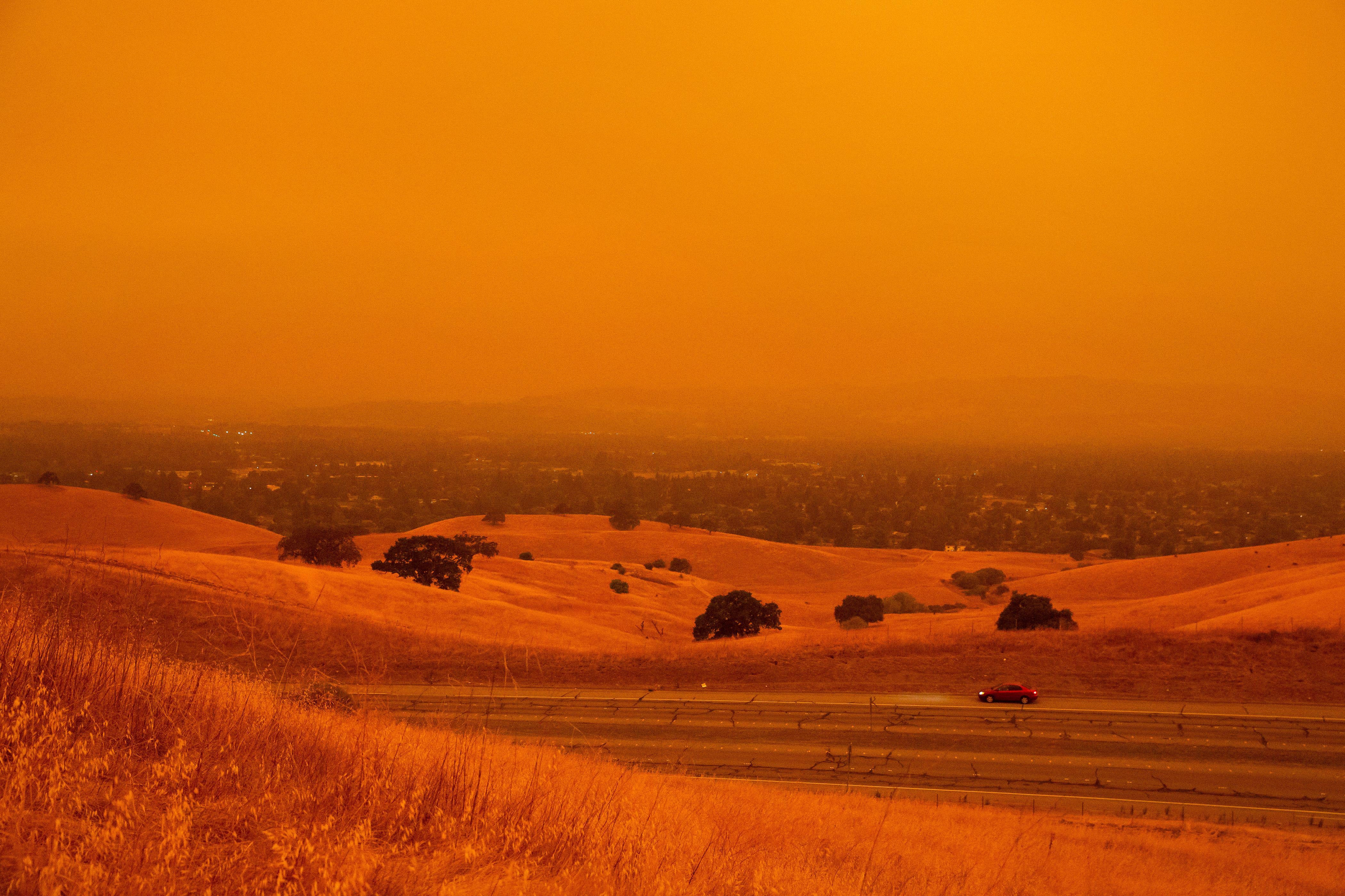 A car drives by in a landscape turned orange-red by wildfire smoke.