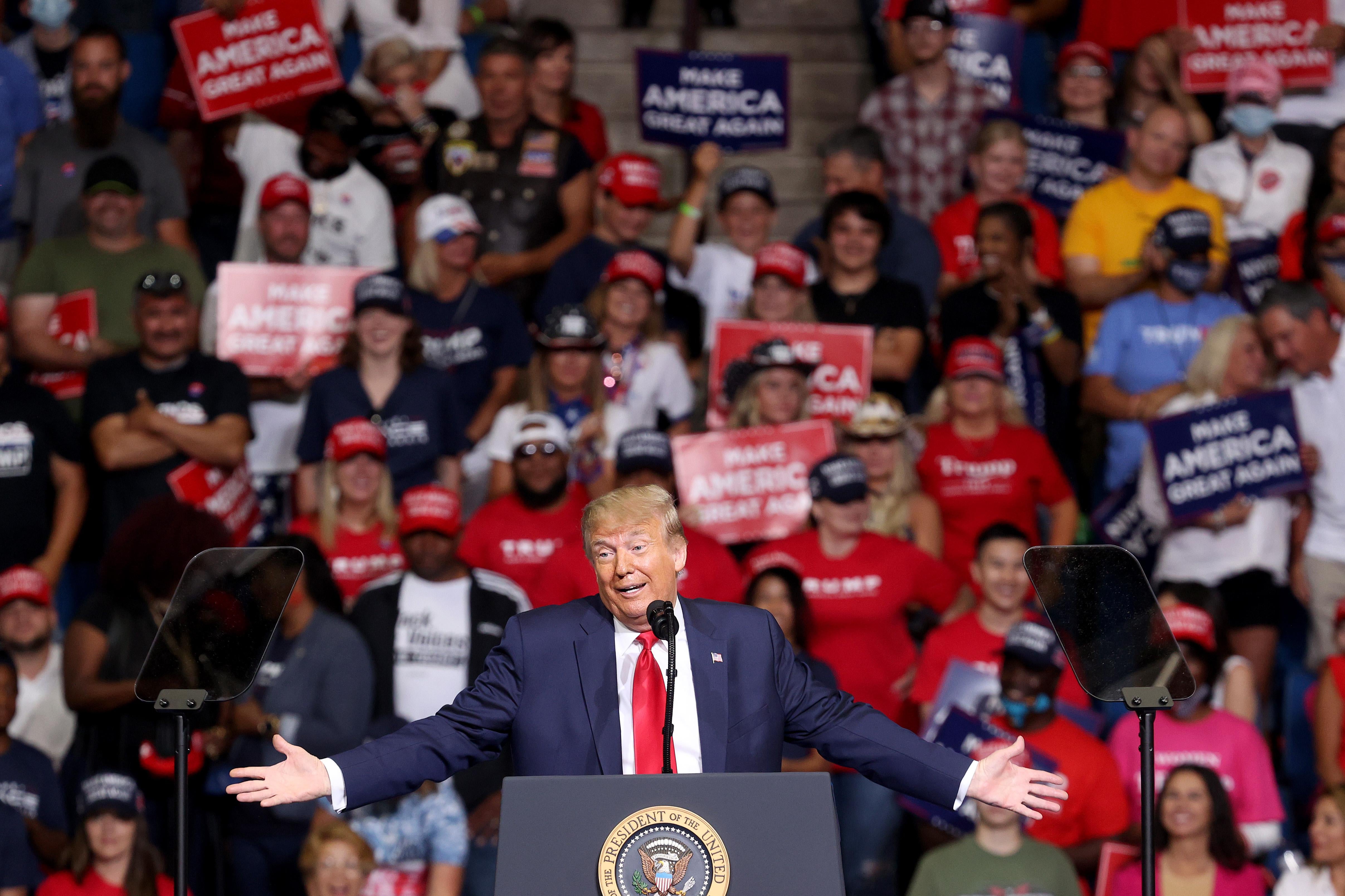 Trump speaks onstage at a podium. Supporters sit in the arena seats behind him.