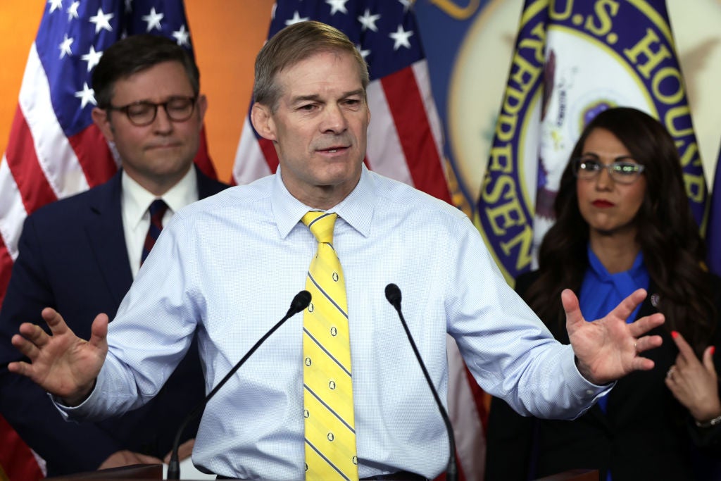 Jordan, wearing a shirt and tie, speaks at a lectern while holding his hands apart in an emphatic gesture. Two other Republican representatives are standing behind him.