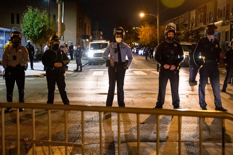 Police wearing riot helmets stand in a row behind a barricade