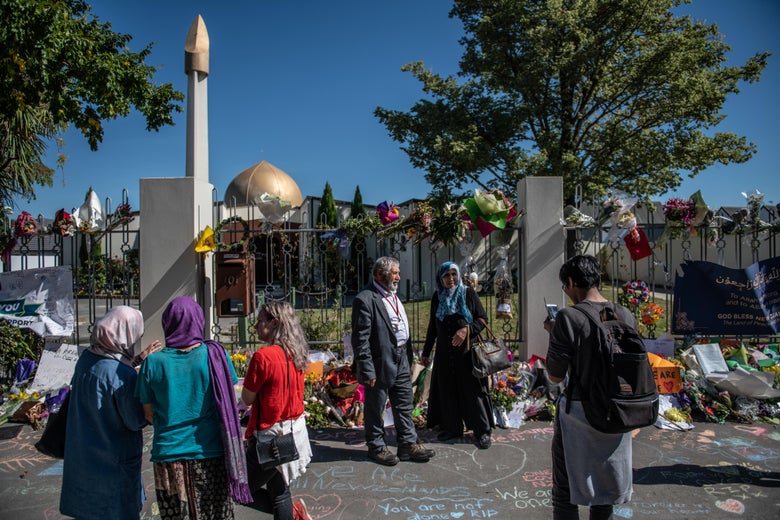 People stand outside the mosque, next to many flowers placed in tribute to the victims of the March 15 attacks.