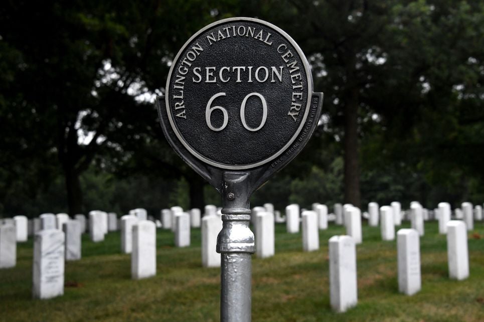 Rows of white headstones stand behind a sign that reads, "Arlington National Cemetery: Section 60."
