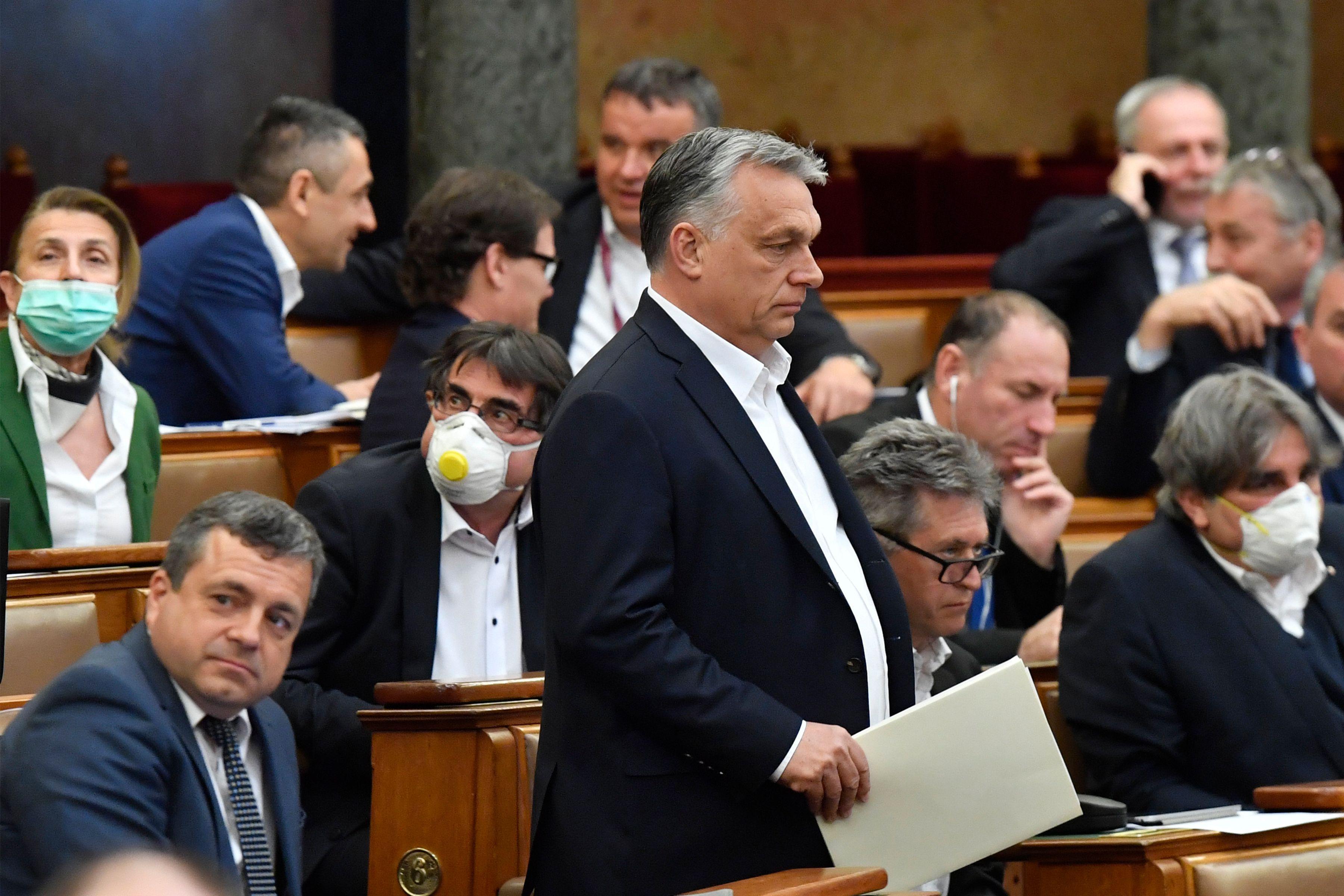 Viktor Orban walks in front of seated members of the Hungarian Parliament, some wearing masks.