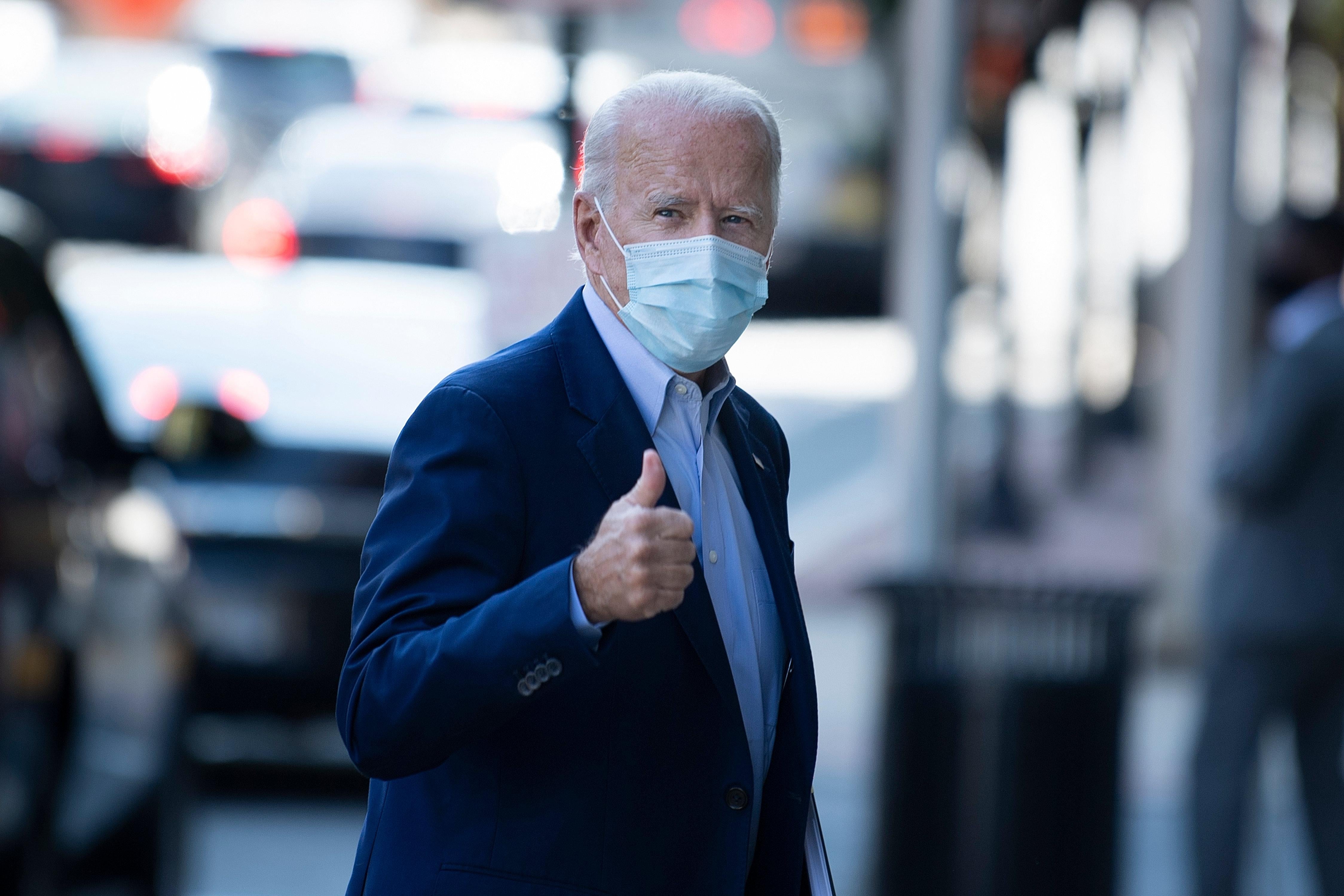 Joe Biden, wearing a mask, gives a thumbs-up as he walks