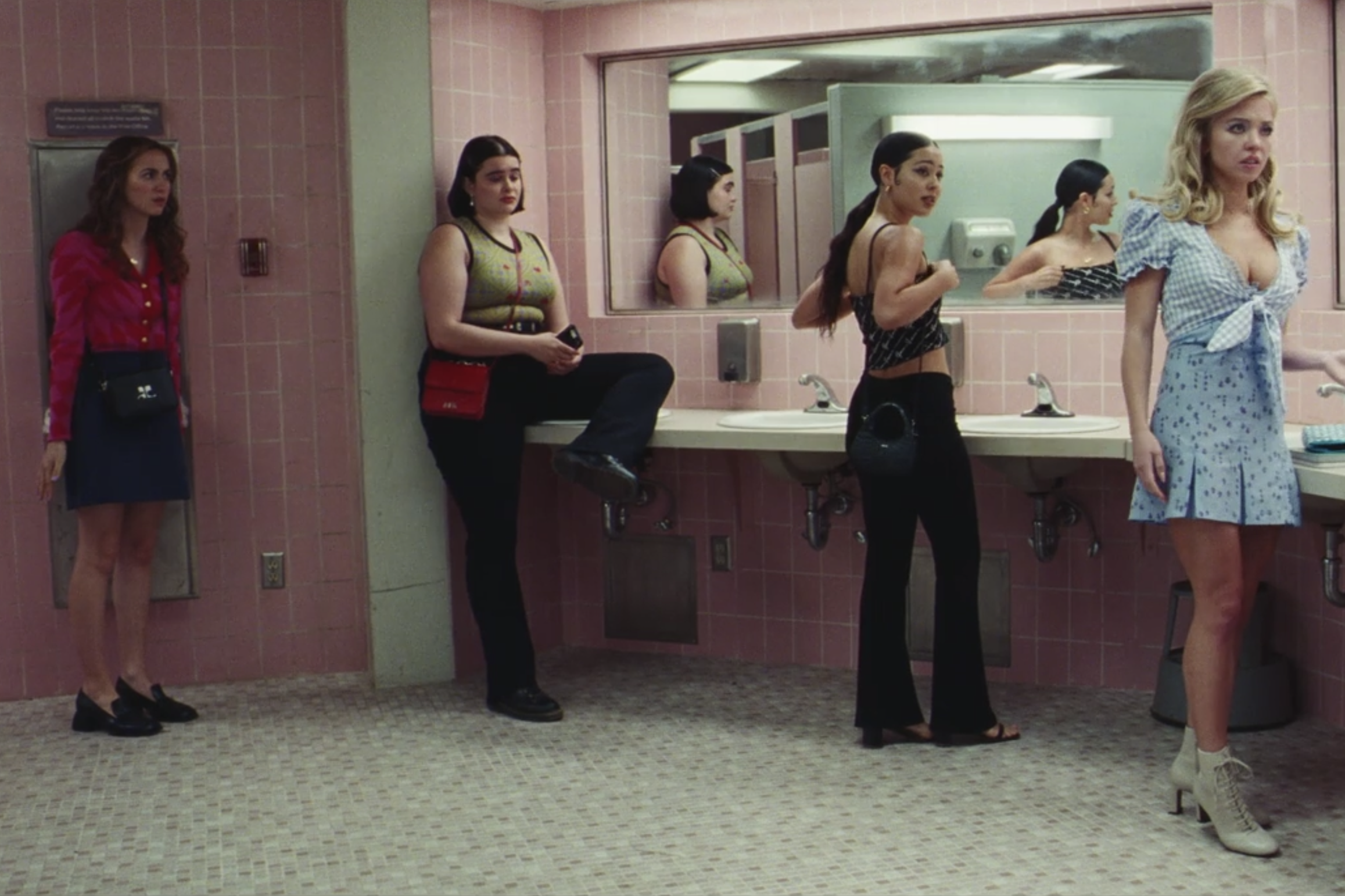 Four girls stand in front of a bathroom mirror, looking to their left. 