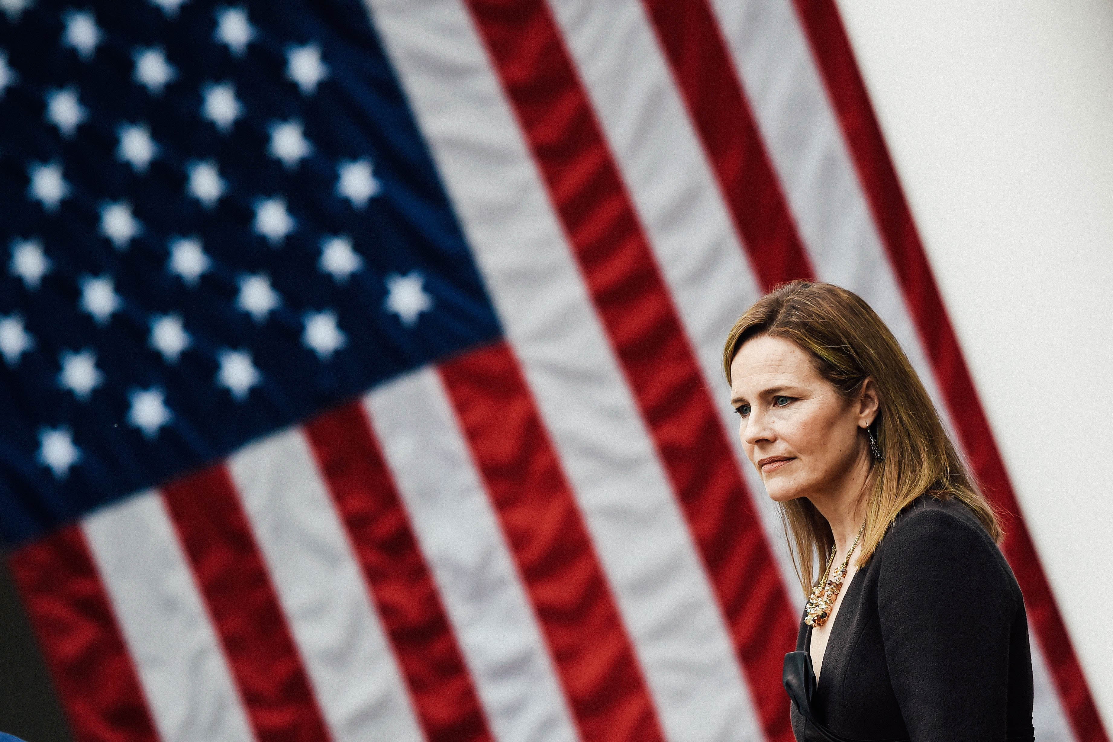Amy Coney Barrett in profile in front of an American flag.