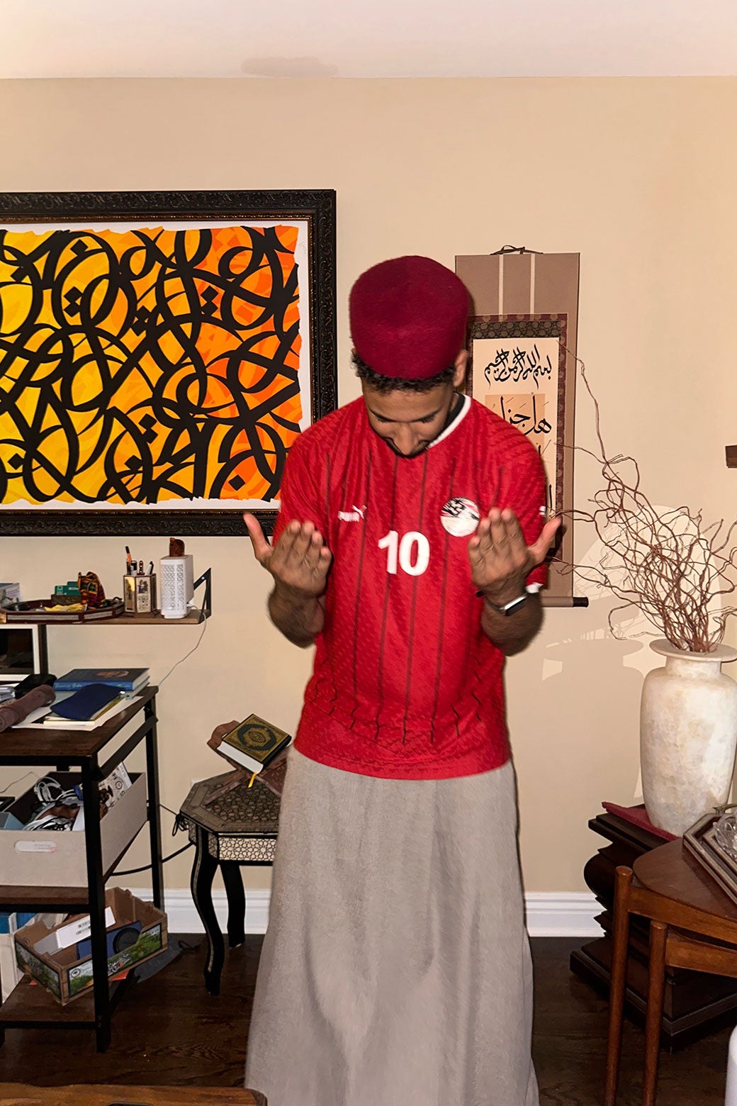 A man is wearing a soccer jersey and a fez-type hat.