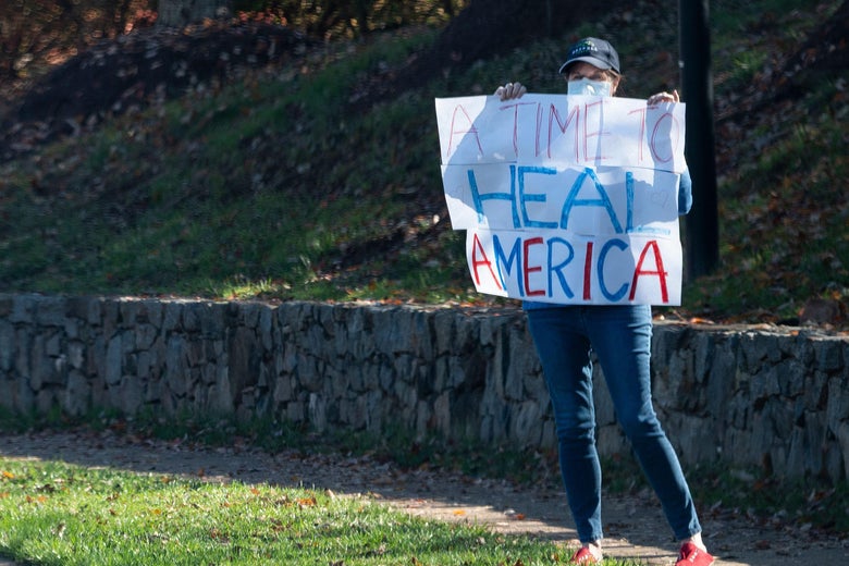 A woman holds up a paper sign that says "A TIME TO HEAL AMERICA" as Trump's motorcade passes