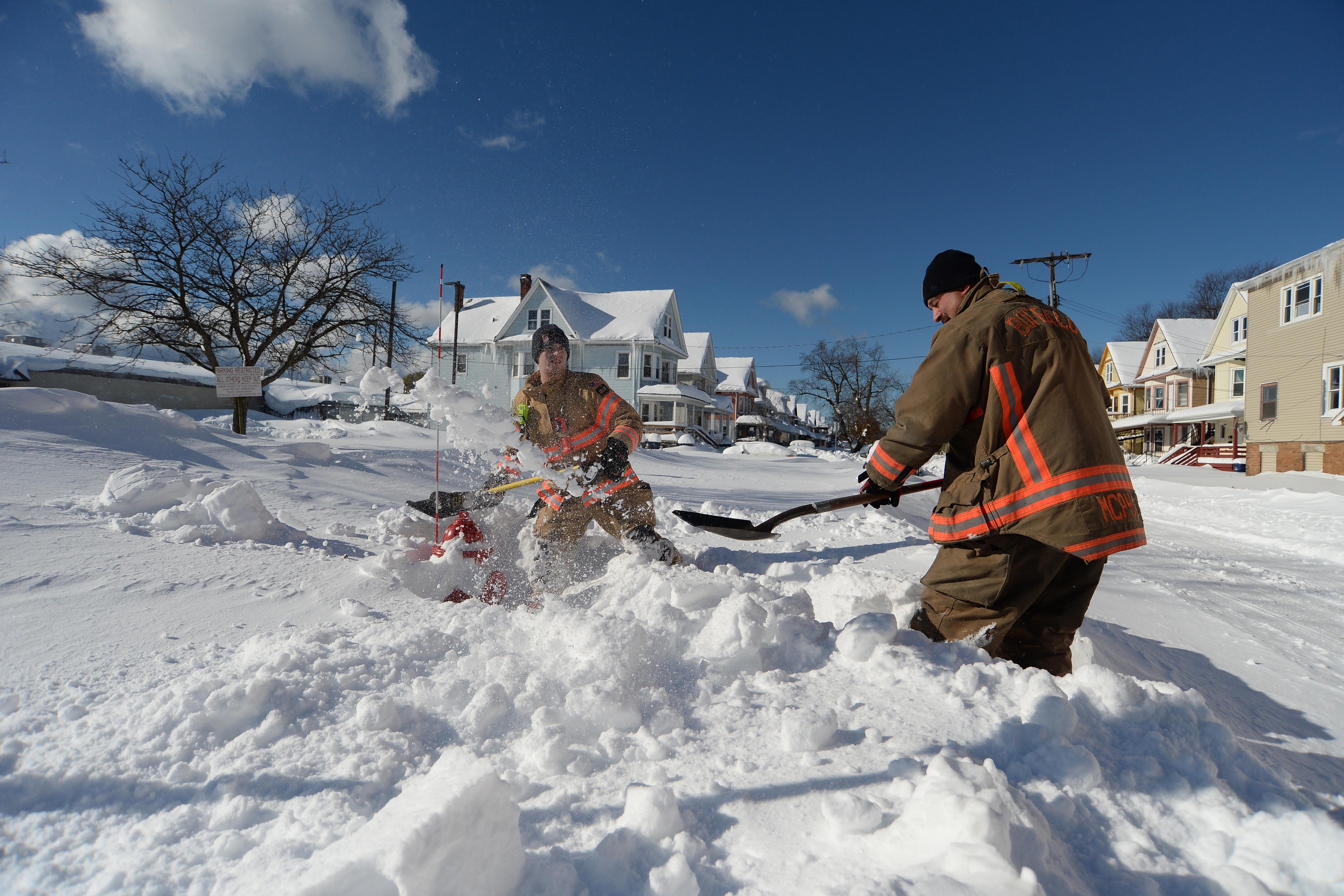 Two firefighters shovel snow.