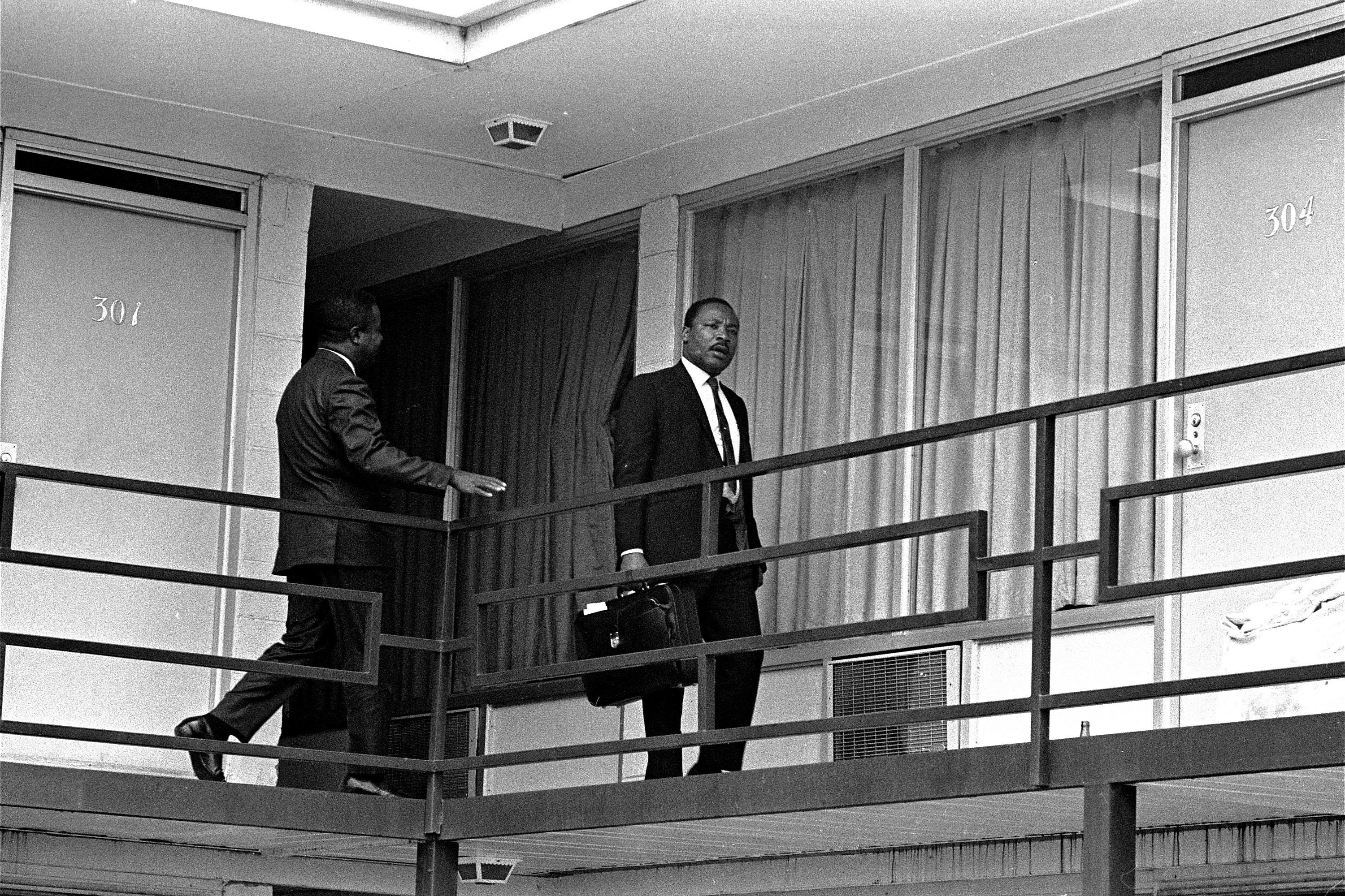 Archival image of MLK holding a suitcase and walking down the exposed hallway of a motel.