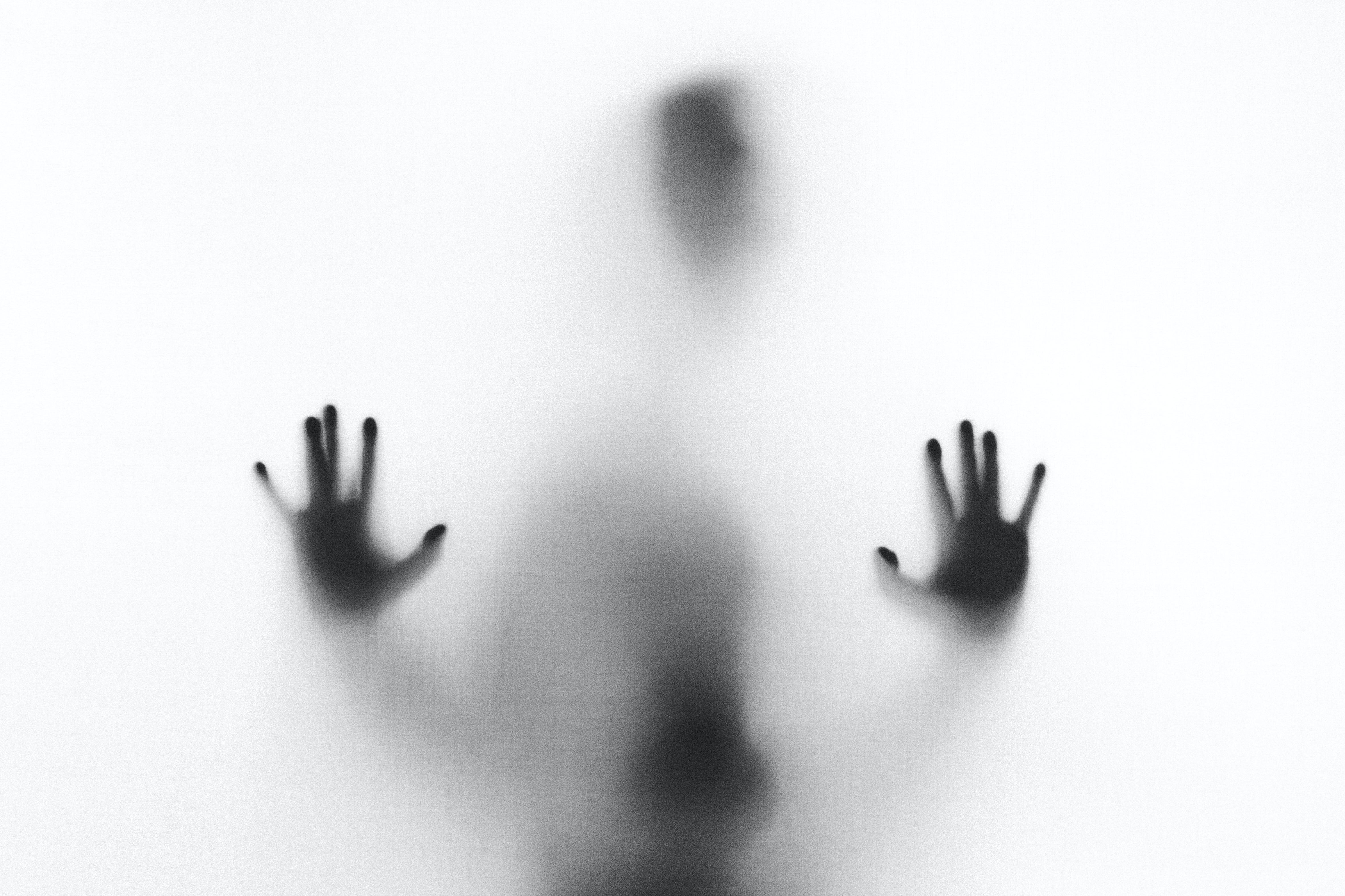 A person stands behind a scrim, their hands placed up against it; you can only see them in shadow.