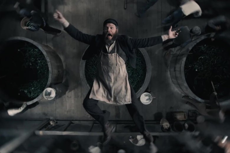An overhead shot of Seth Rogen, in costume as a 1920s factory worker, falls backwards into a giant vat of pickles, arms outspread, screaming.
