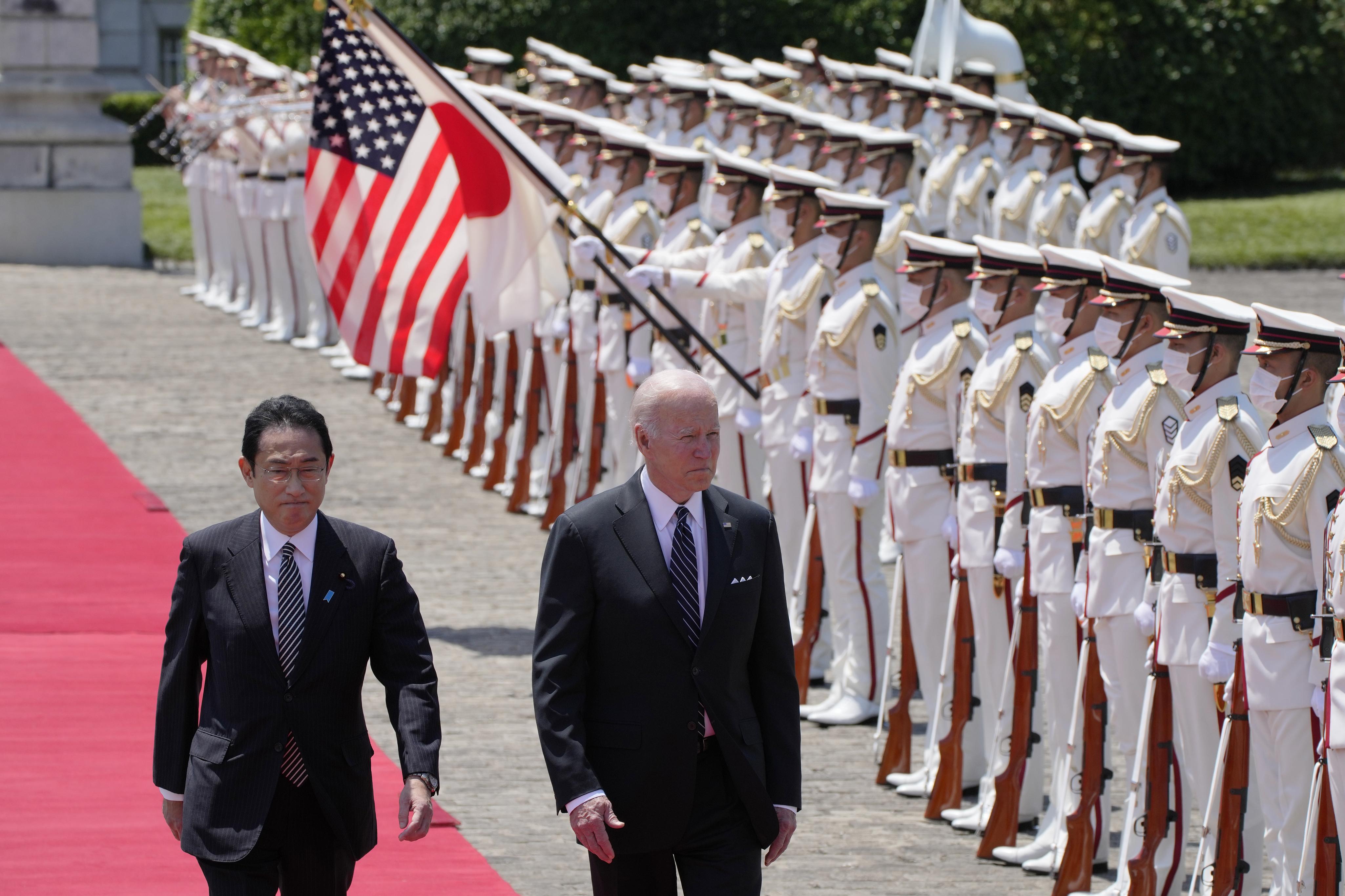 Kishida and Biden walk down a red carpet in front of members of the Japanese military in white uniforms.