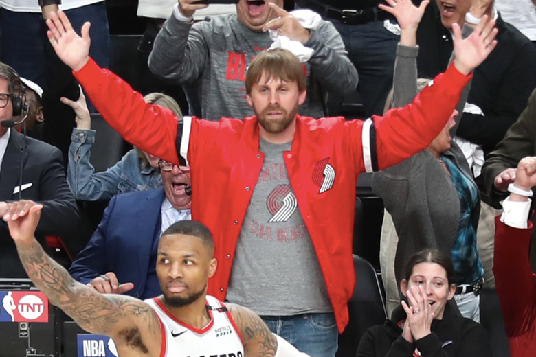 A bearded fan in a red Blazers jacket spreads his arms serenely behind Lillard.