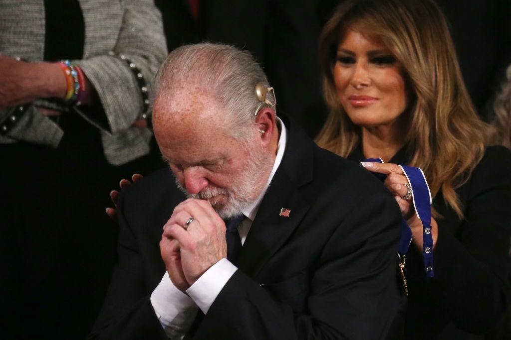 Limbaugh bows his head and clasps his hands together as Melania Trump stands behind him and prepares to put the medal around his neck.