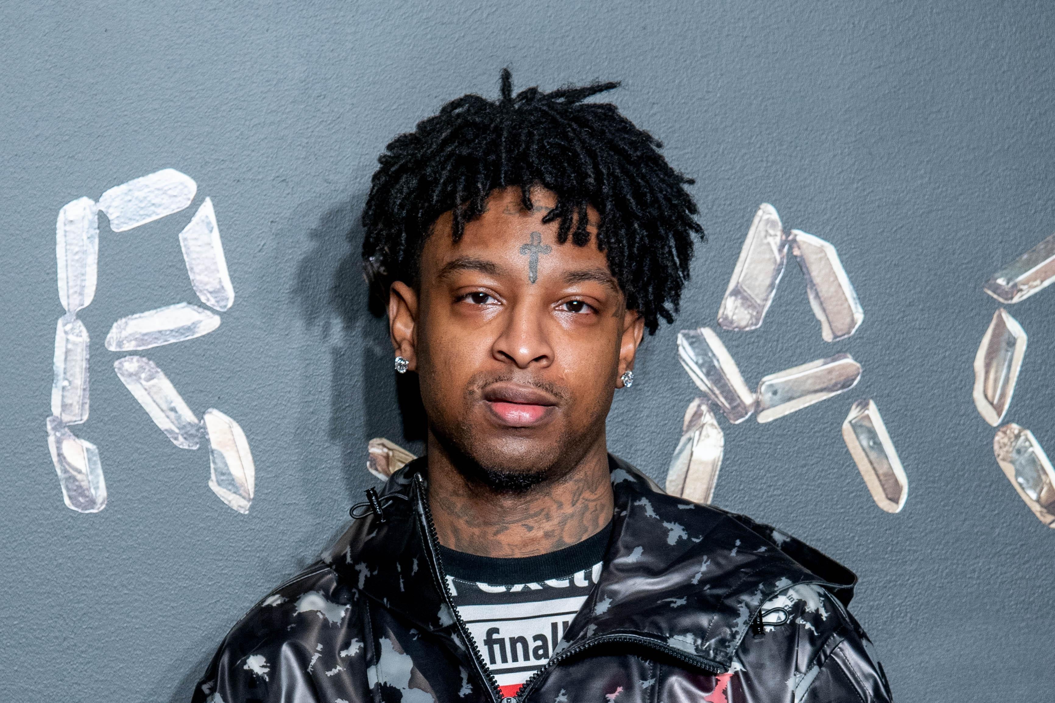21 Savage standing in front of a sign reading "Versace."