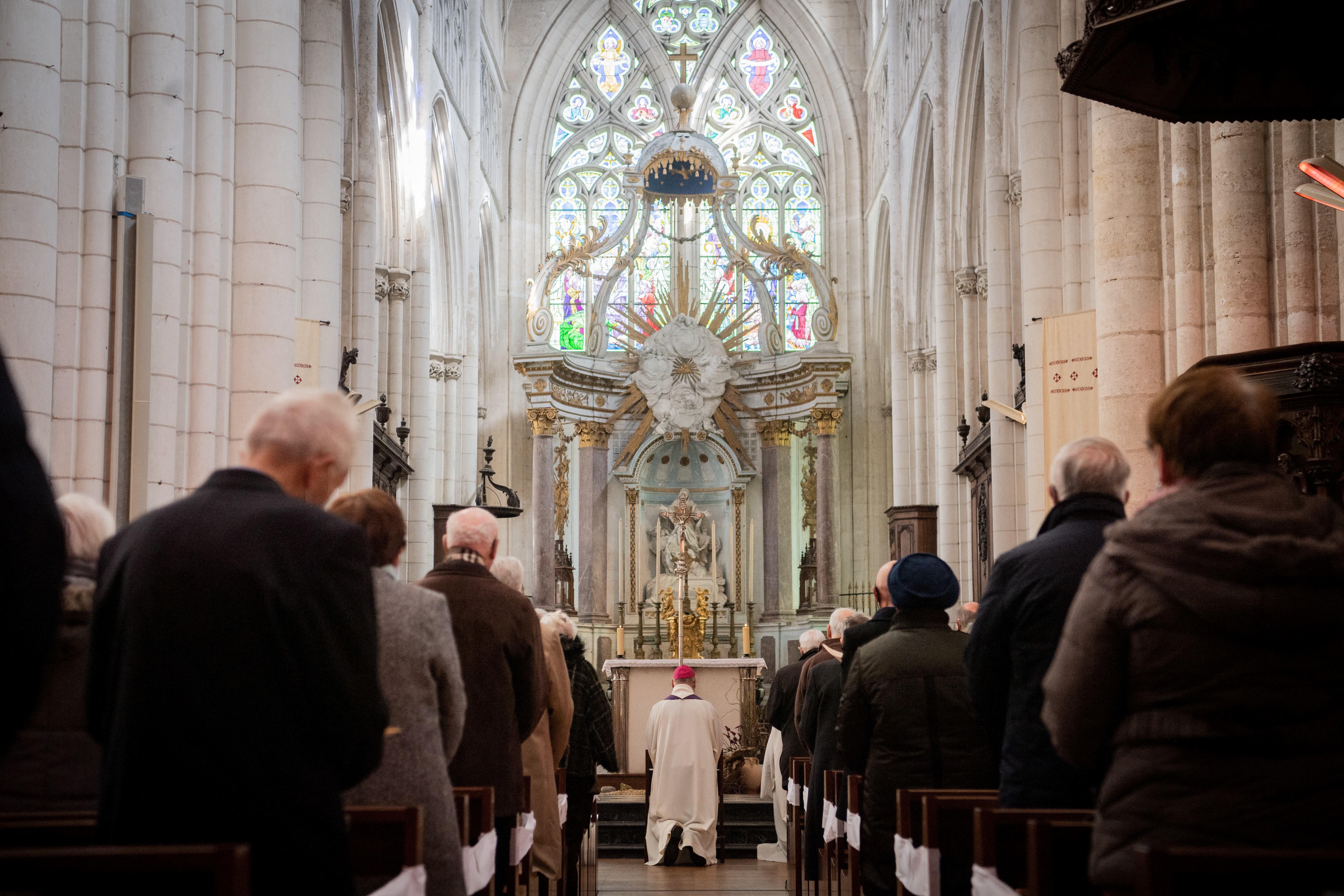 A bishop kneels in front of an alter in a crowded church.