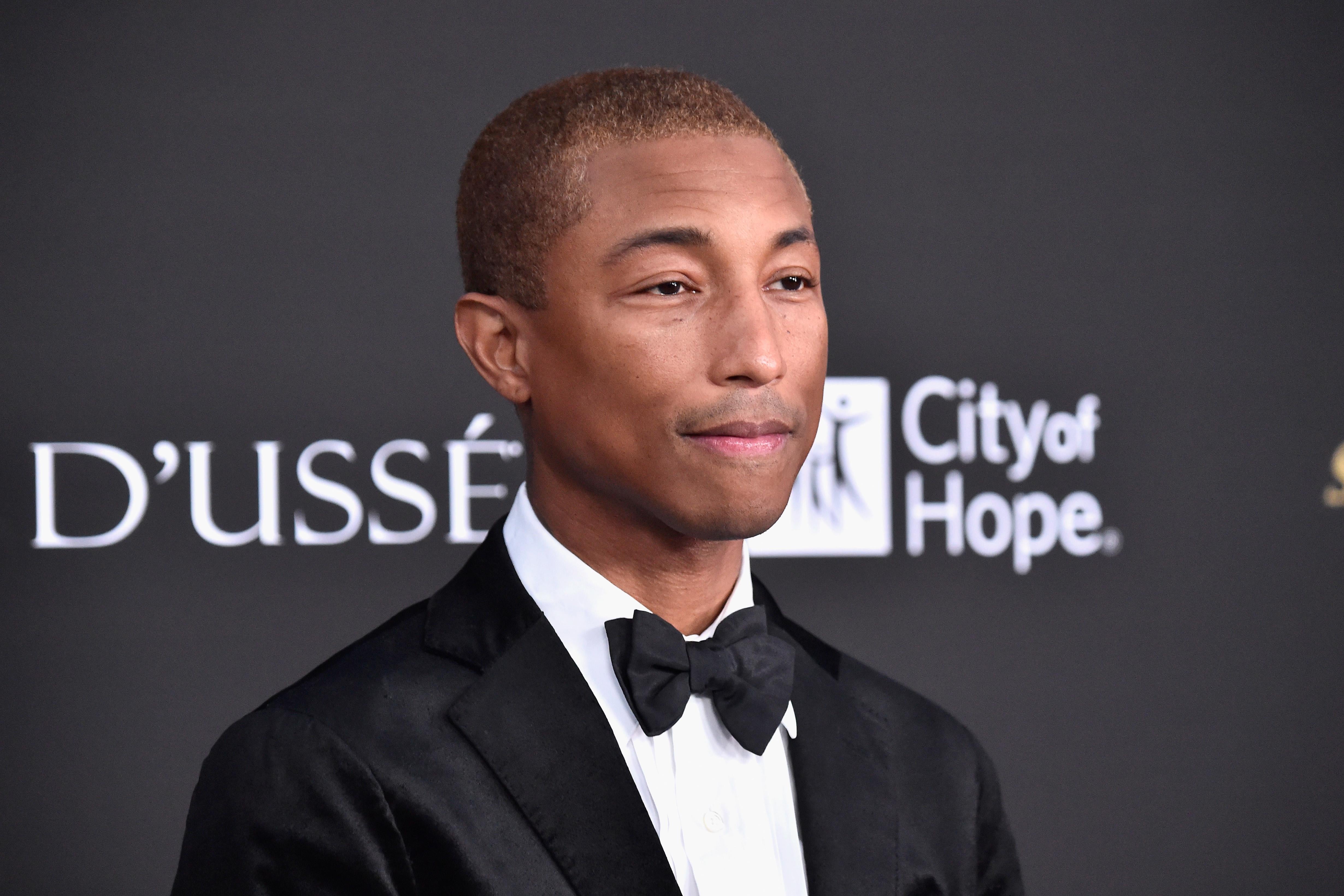 Pharrell Williams wears a black suit and bowtie.