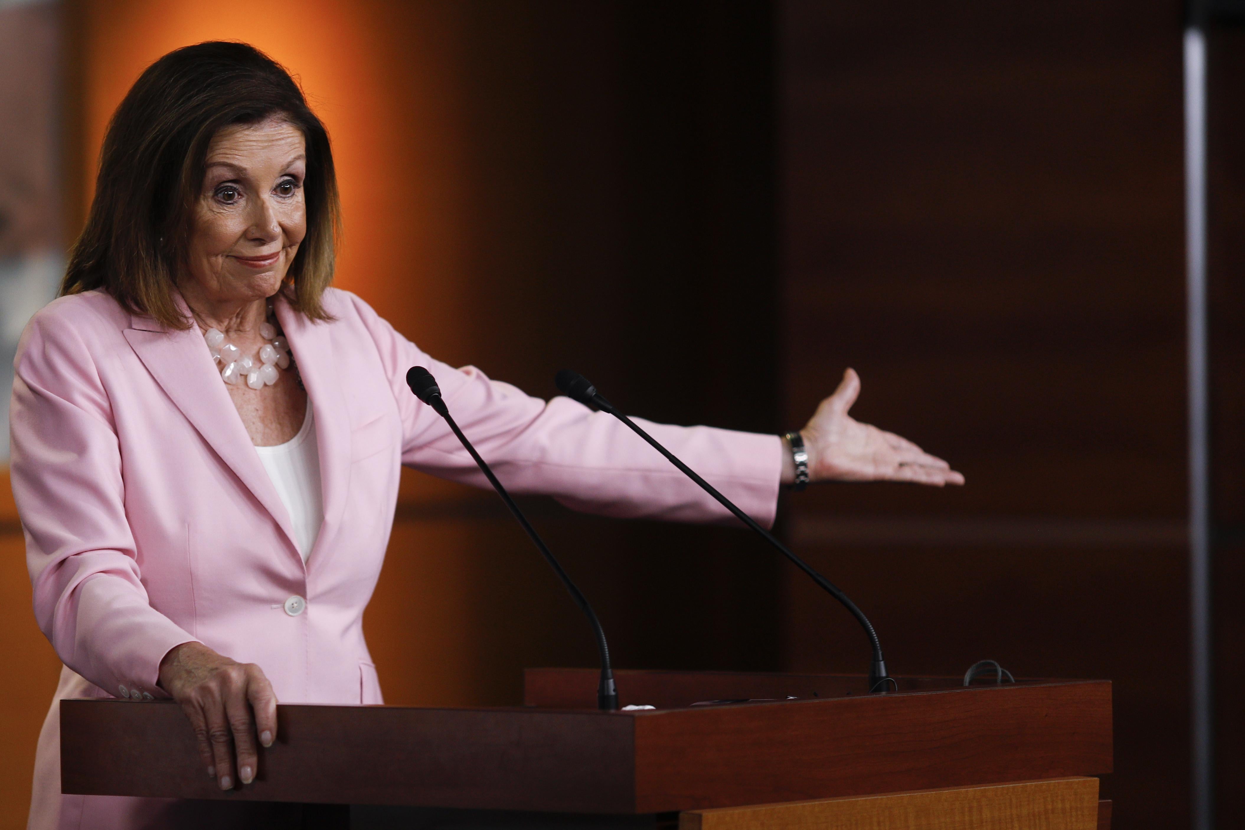 Nancy Pelosi gestures while behind a podium.