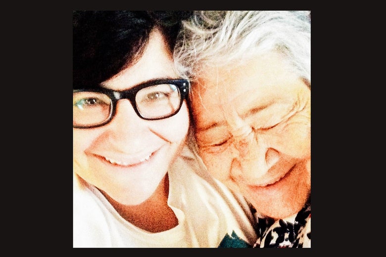 A younger woman with dark hair and black glasses holds an older woman with white hair close.