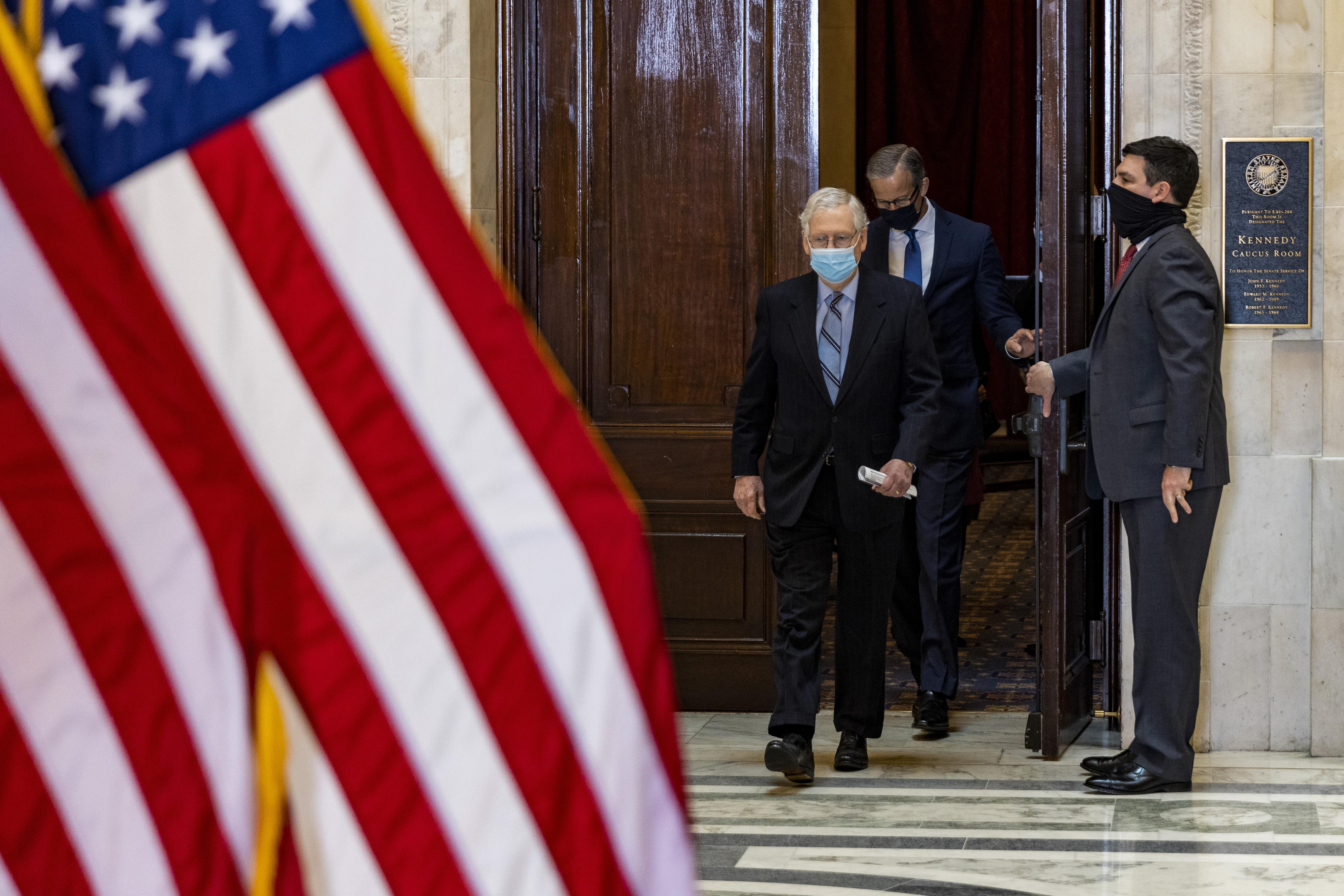 A man wearing a face mask opens a door to let in McConnell and another man, both of whom are wearing face masks. A U.S. flag is seen in the foreground.