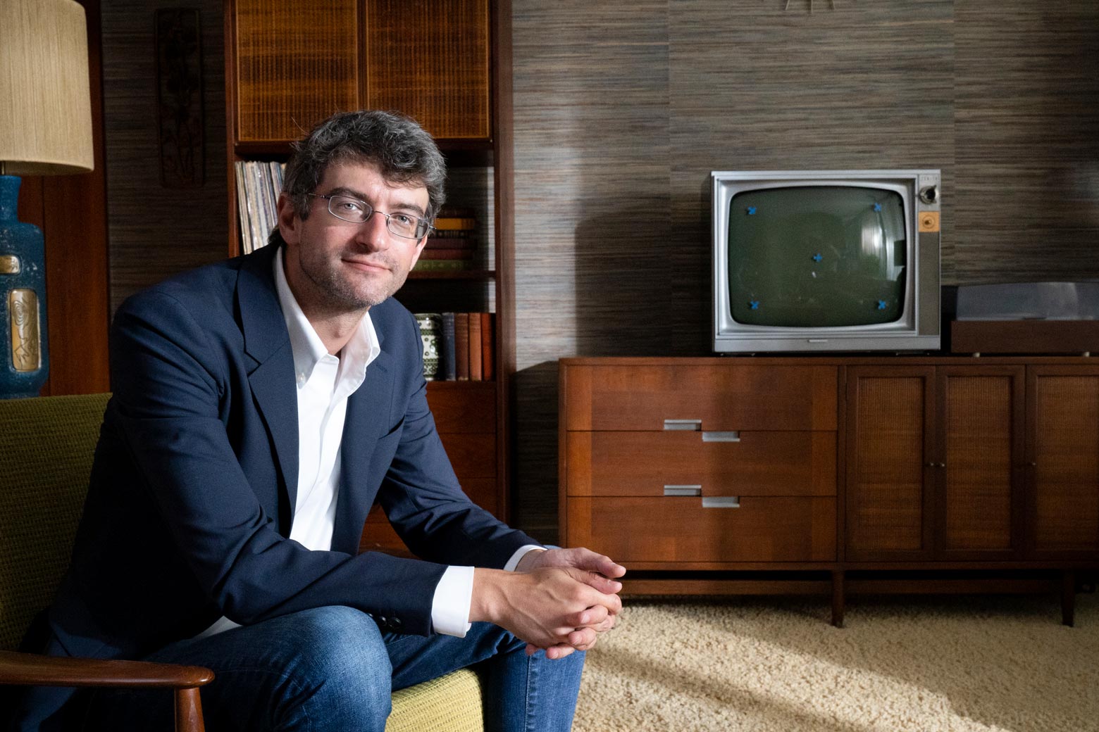 Leon Neyfakh sits in a chair in front of a credenza and old-fashioned TV.