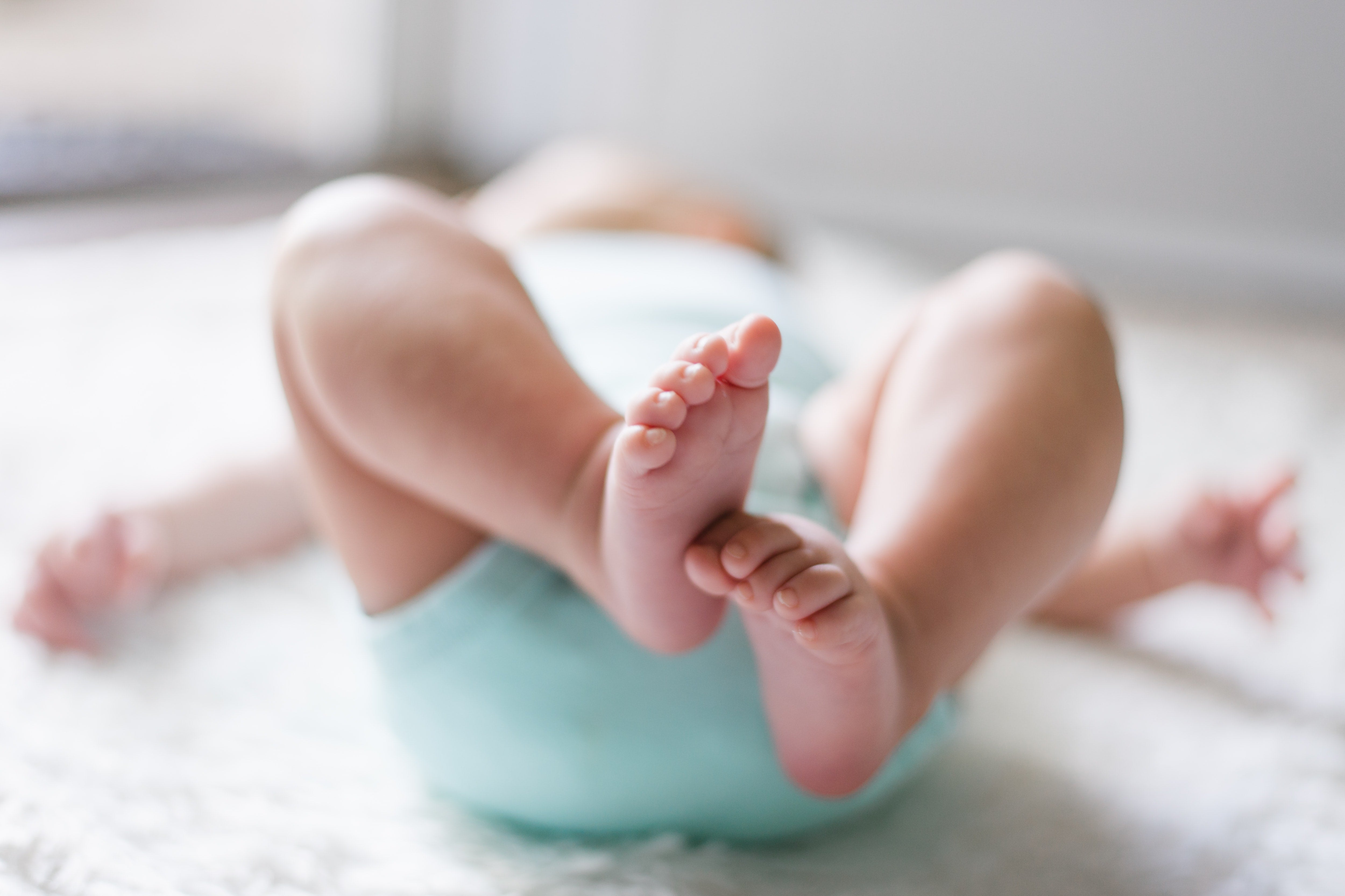 A baby lying down on a white blanket. Only the baby's feet are clearly visible, the rest of the baby is out of focus. 