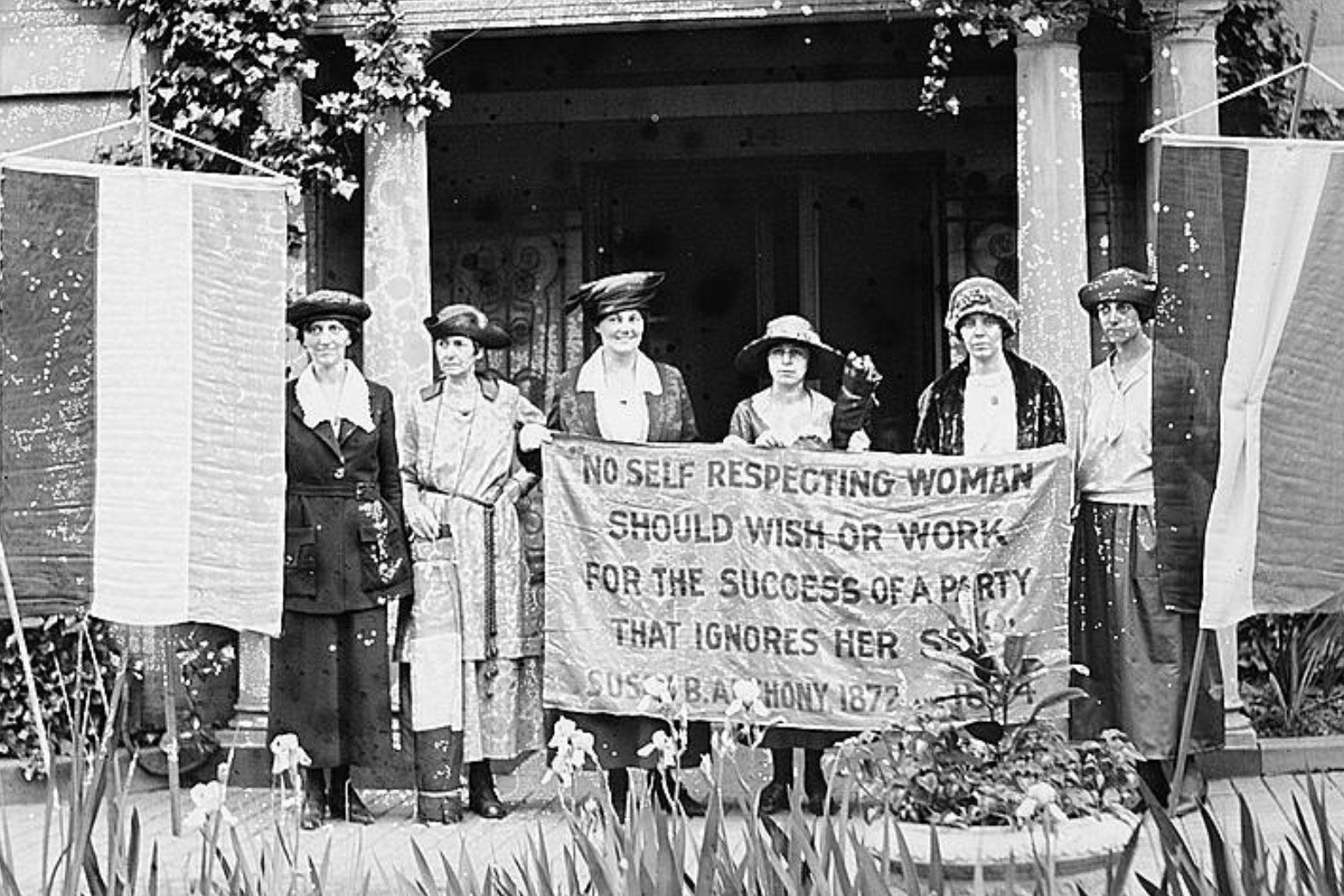 Suffragists Sue White, Benigna Green Kalb, Jas Rector, Mary Dubrow, Alice Paul, and Elizabeth Kalb stand in front of the National Woman’s Party Washington HQ holding a sign with a Susan B. Anthony quote.