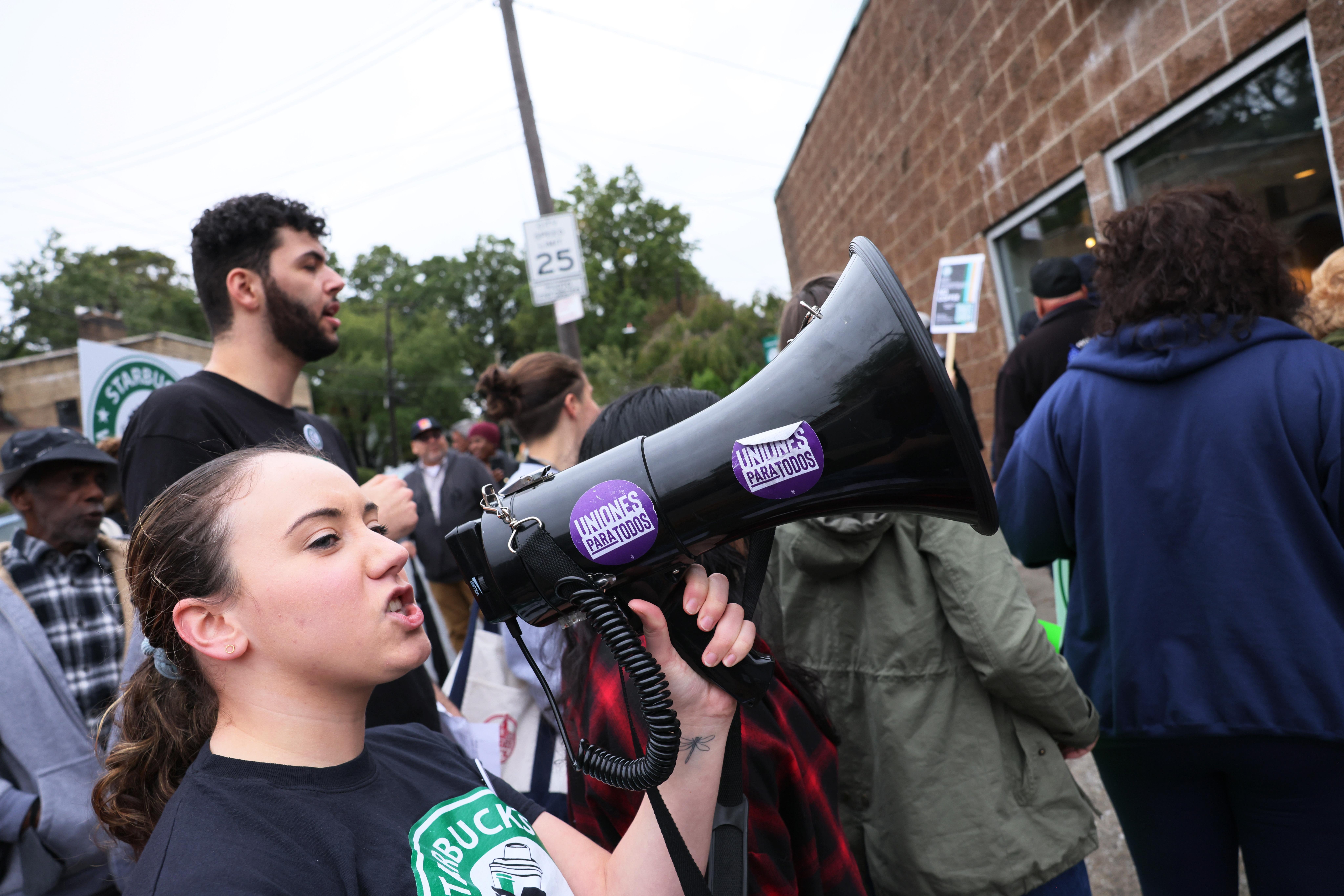 A woman in a Starbucks Union T-shirt speaks into a megaphone with other workers holding signs around her