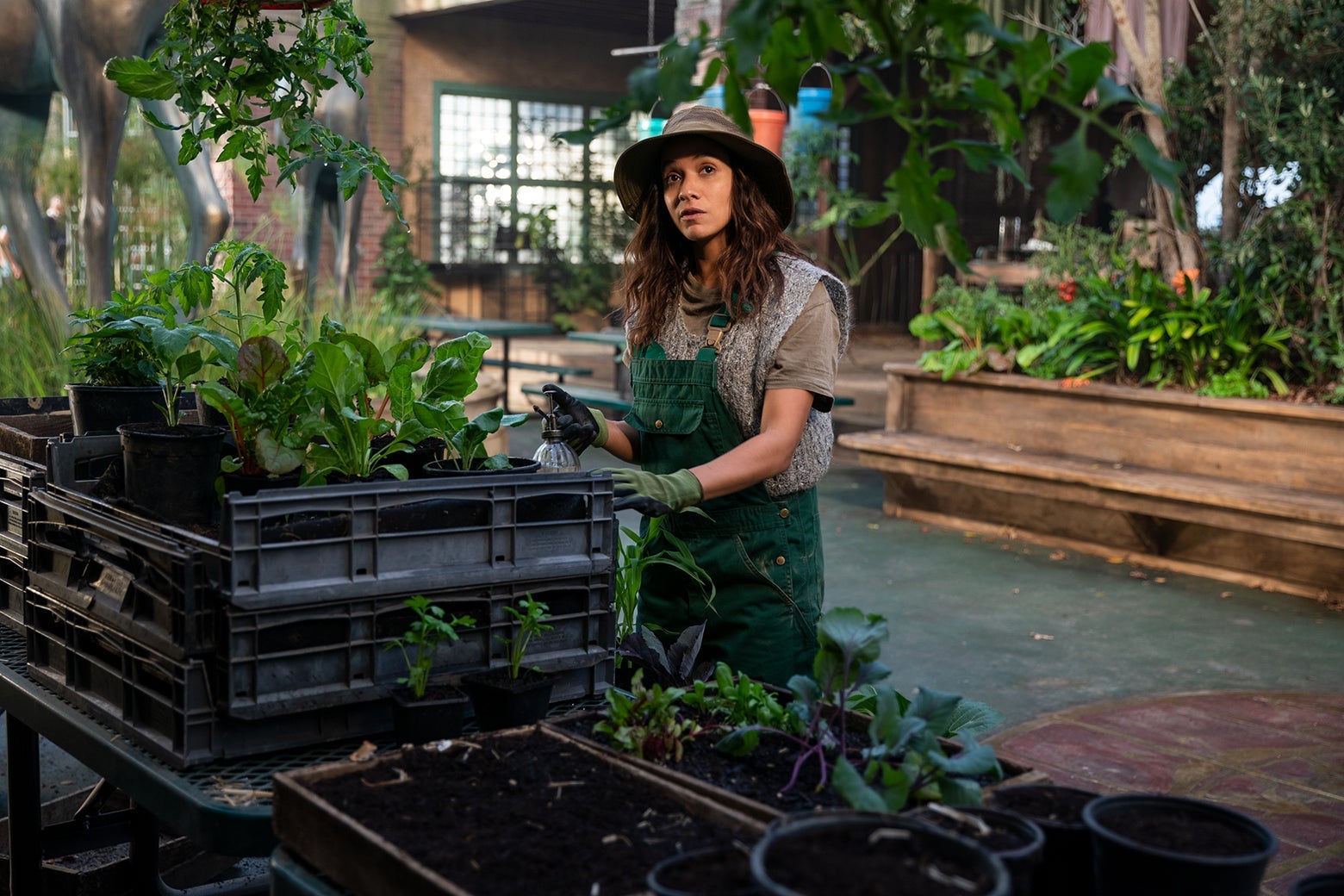 Actress Dania Ramirez, wearing a floppy hat and gardening apron, tends to some seedlings in a still from Sweet Tooth.