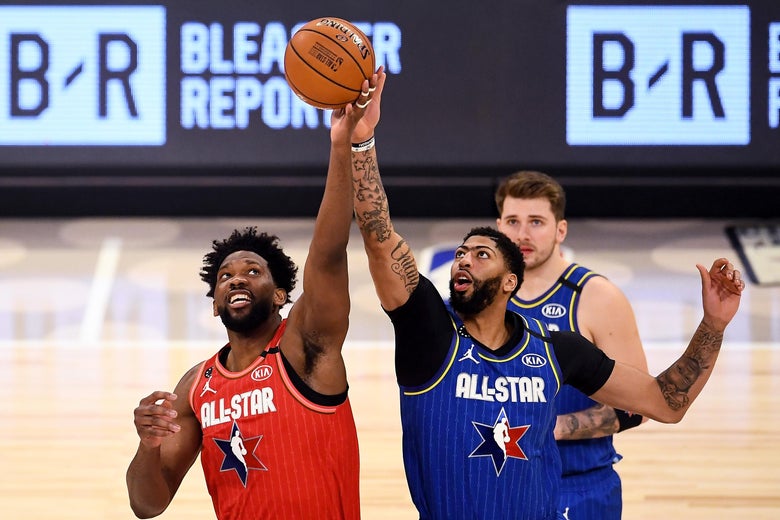 Joel Embiid and Anthony Davis battle for a tip-off during the NBA All-Star Game; Luka Doncic looks on in the background.