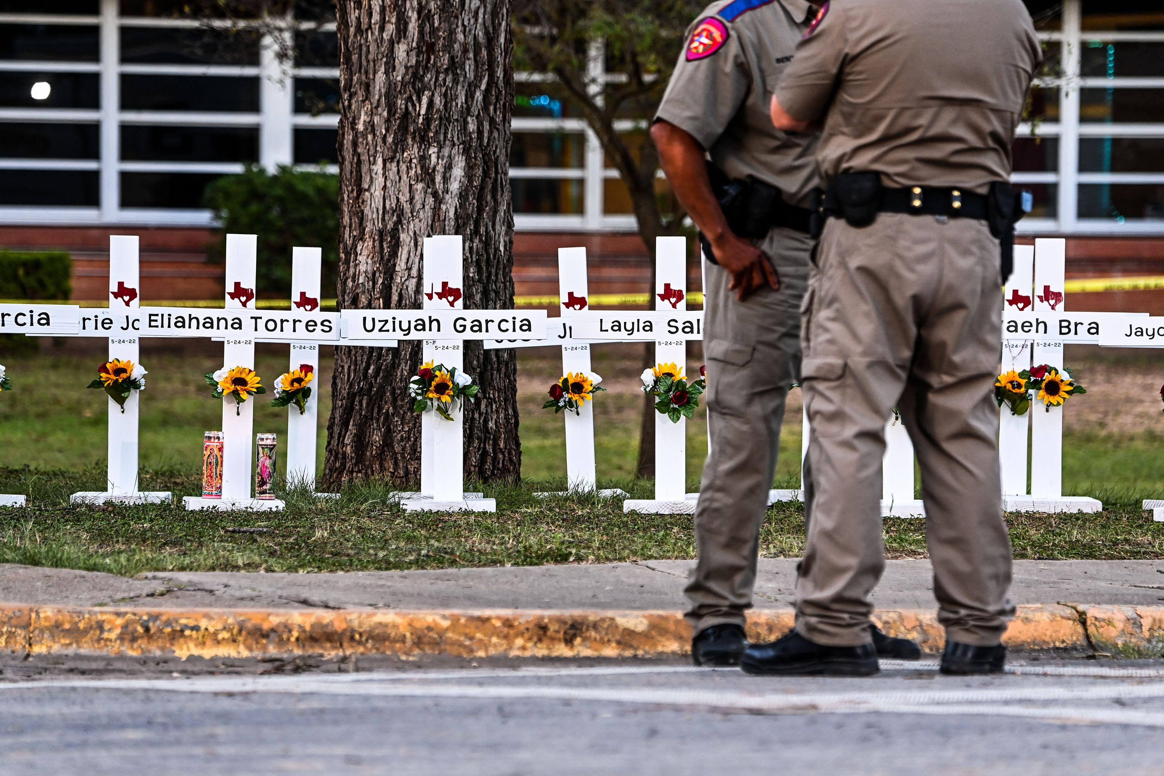 Police officers stand near a makeshift memorial for the shooting victims at Robb Elementary School