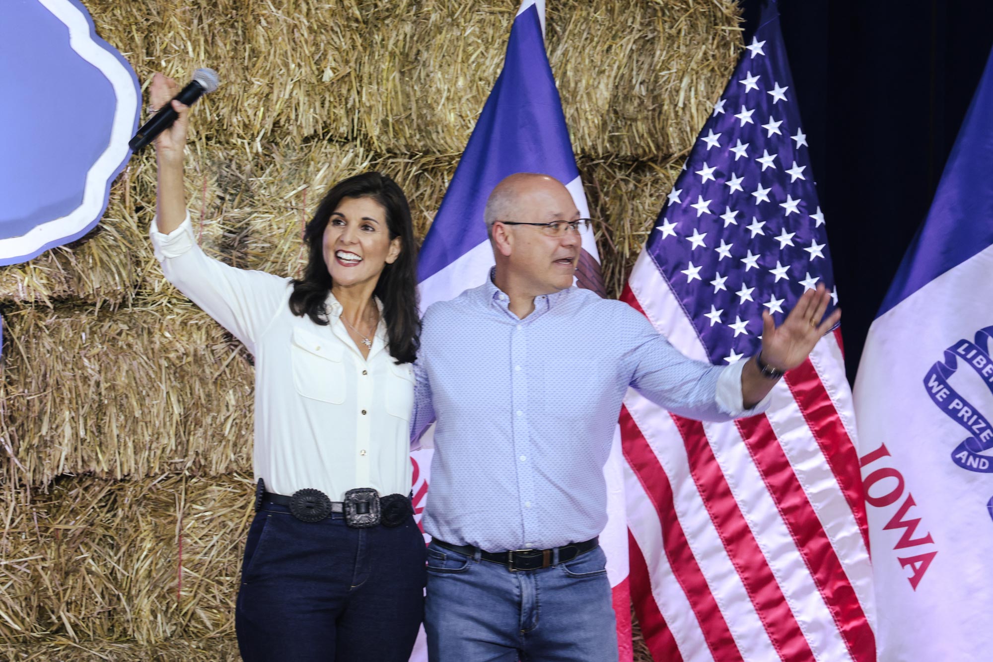 Nikki Haley and her husband stand and wave in front of a stack of hay and the American and Iowa flags.