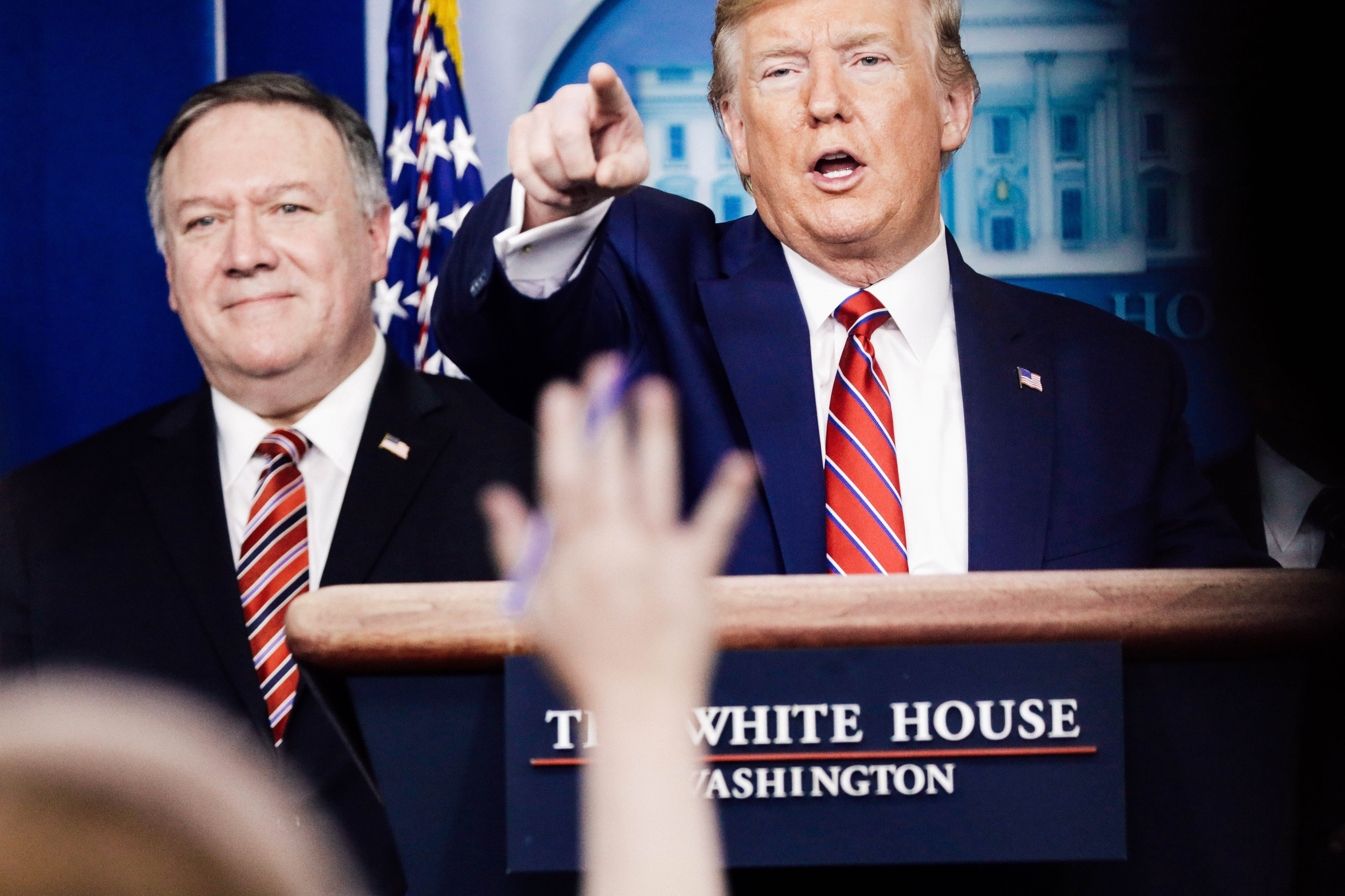Donald Trump, standing at a lectern, stands next to Mike Pompeo and points over a raised hand.