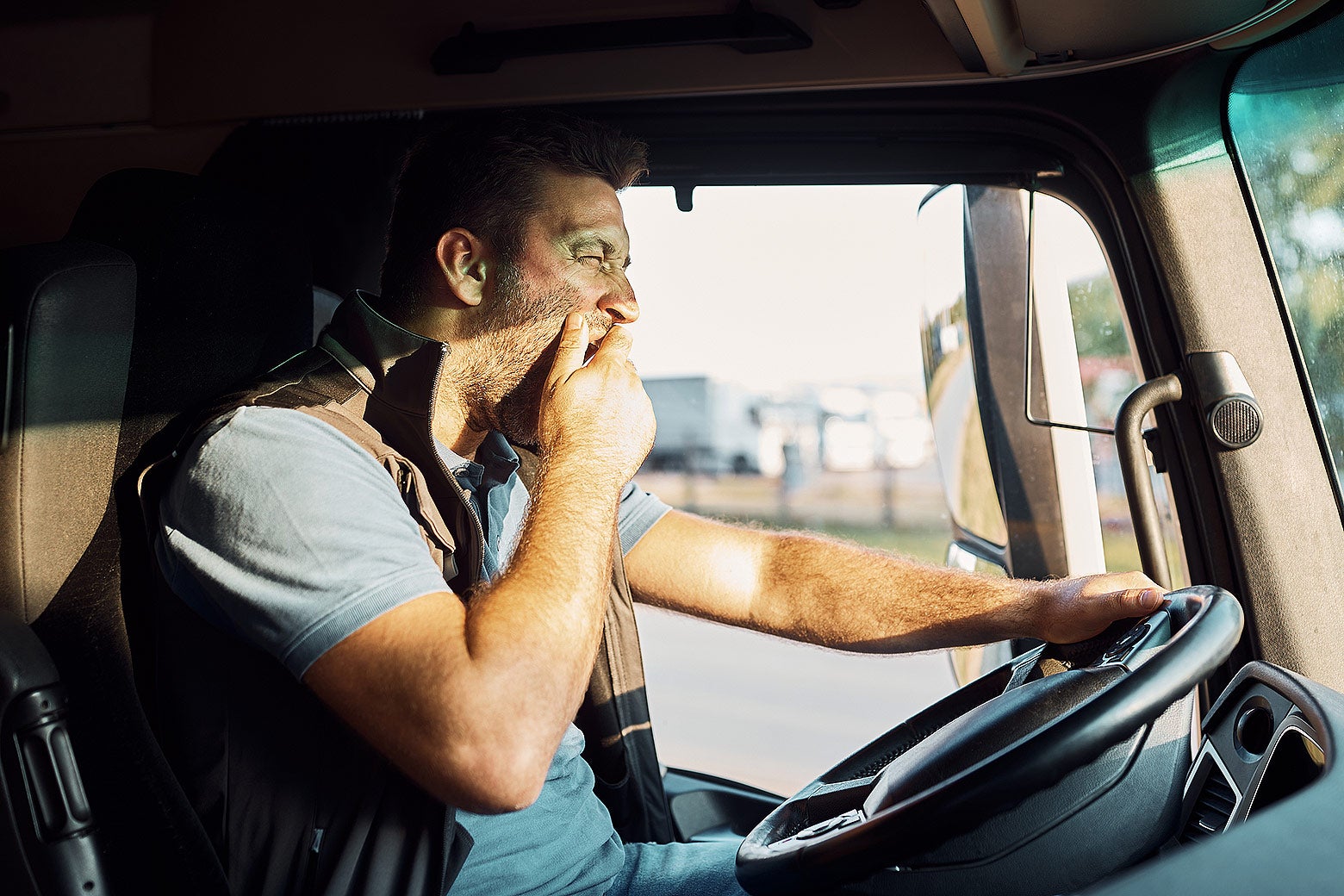 A driver behind the wheel of a truck yawns.