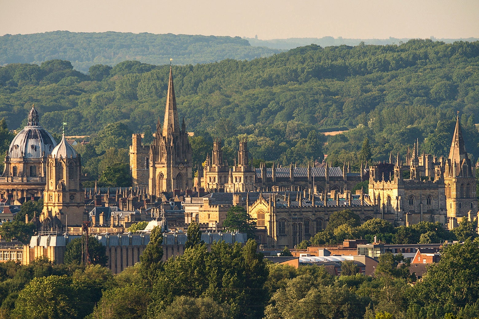 Oxford's medieval spires amid wooded hills on a sunny day.