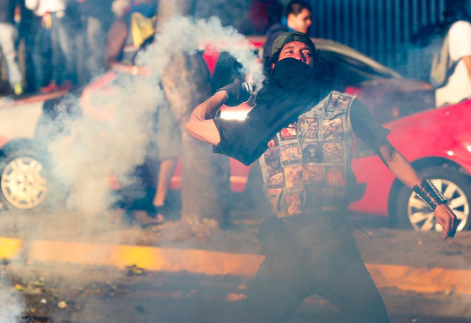 An opposition demonstrator throws a gas canister back to riot police during a protest against President Nicolas Maduro's government in Caracas.