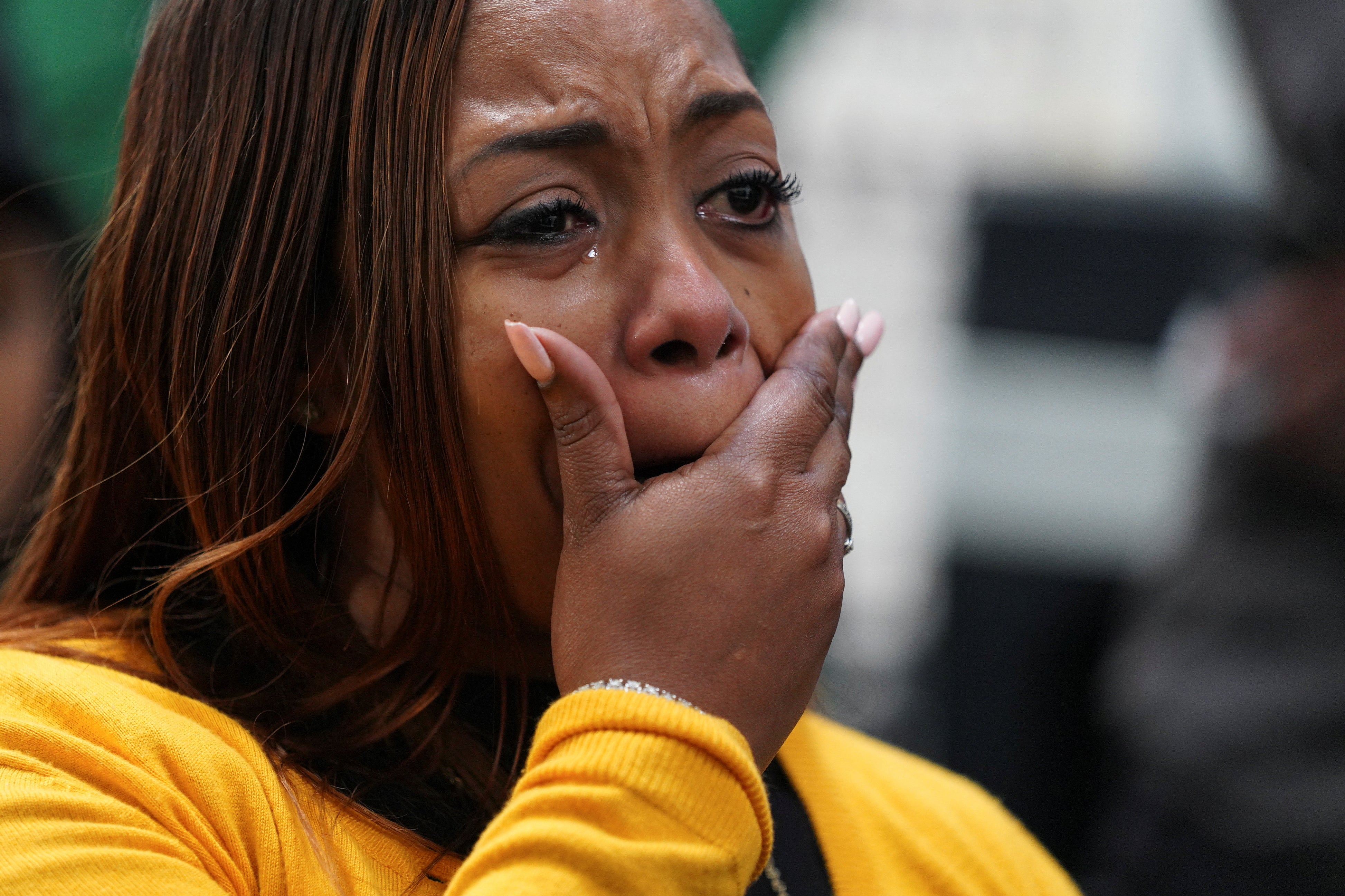 A woman holds her hand over her mouth, shocked, as she cries.