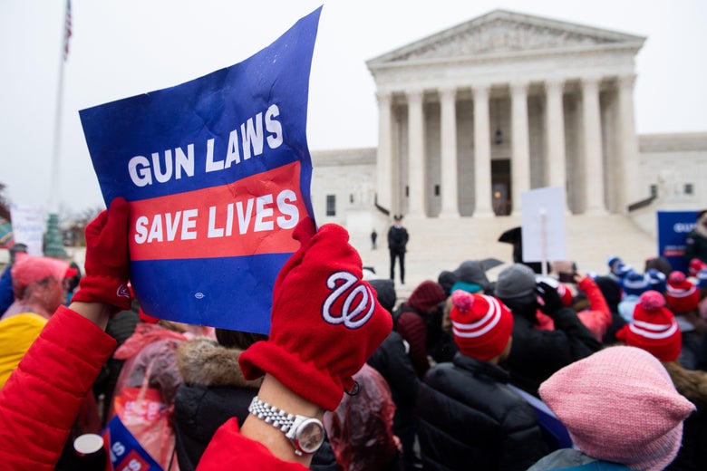Person wearing a Washington Nats glove holds a sign that says "Gun Laws Save Lives" amid a crowd of gun control activists