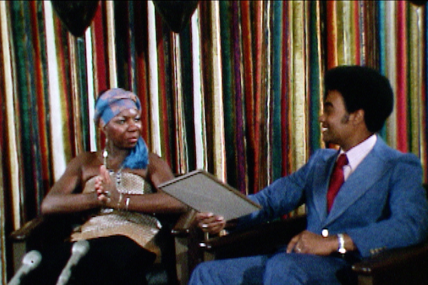 Nina Simone, in a gold lamé dress and blue headscarf, sits beside Warren Widener.