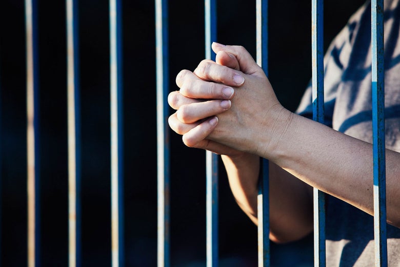 Woman's hands slipping through jail cell bars.