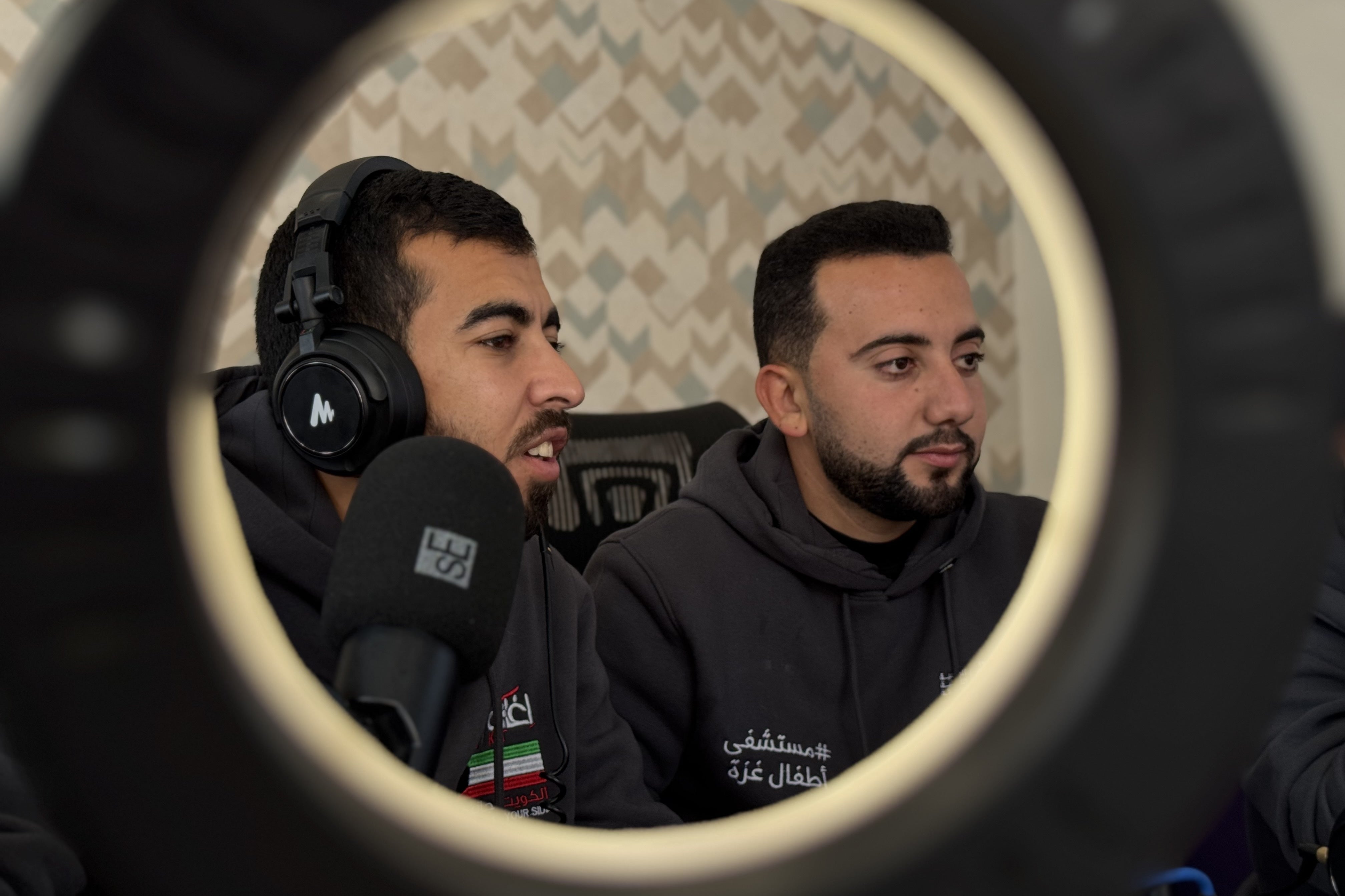 Dos jóvenes palestinos transmiten en vivo frente a cámaras, micrófonos y un anillo de luz.