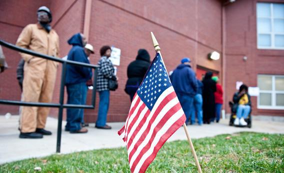 An American flag flutters in the grass as voters wait in line to cast their vote.
