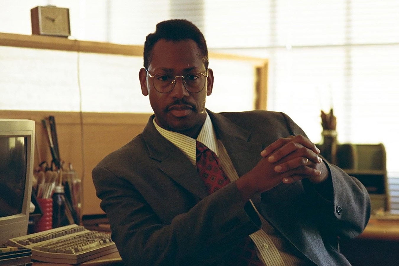 A Black man in an ’80s-era suit and wire-rimmed glasses looks ahead intently.
