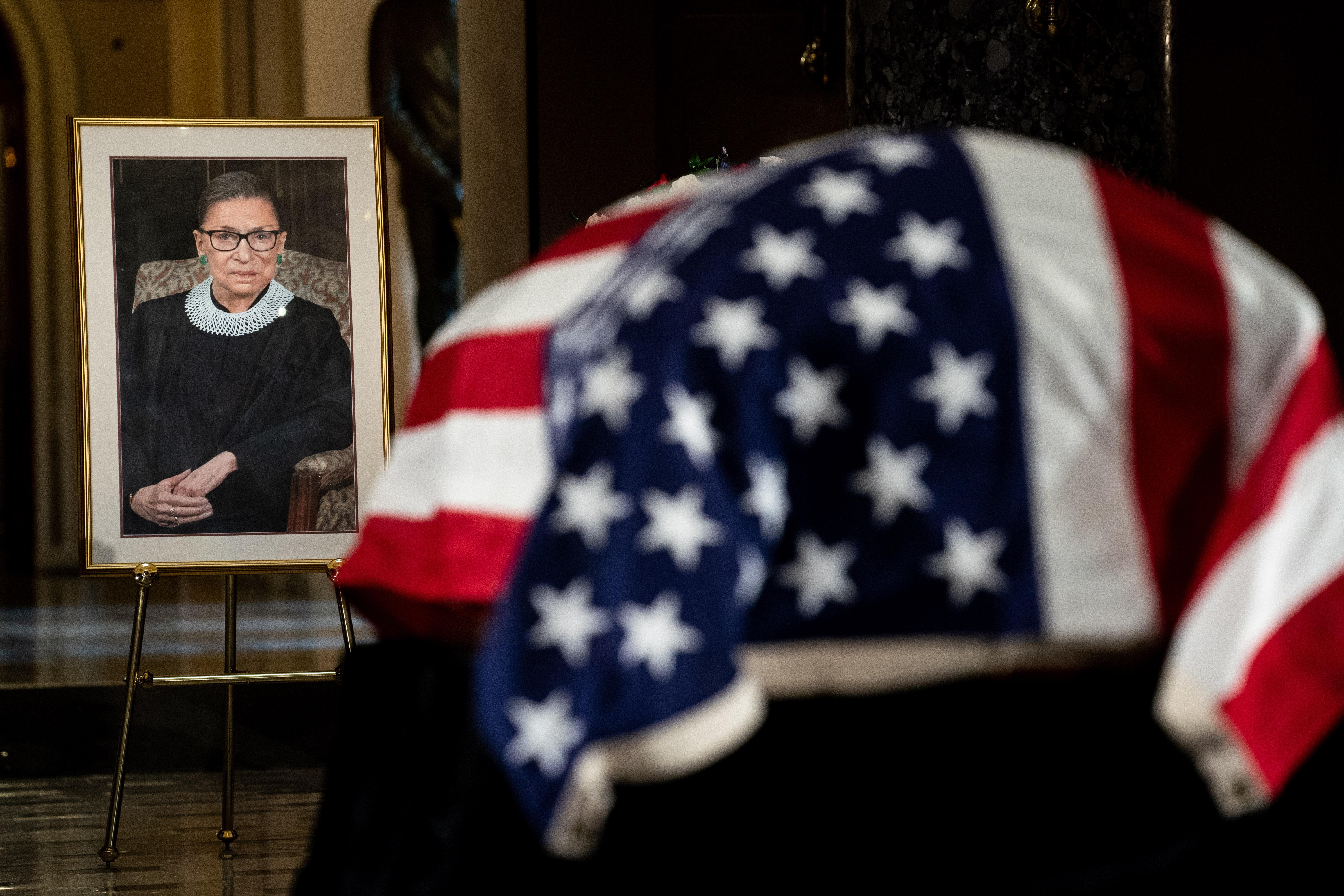 The flag-draped casket of RBG is seen near a framed portrait of her.