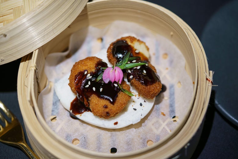 Chicken with brown sauce garnished with a pink flower in a bamboo steamer.