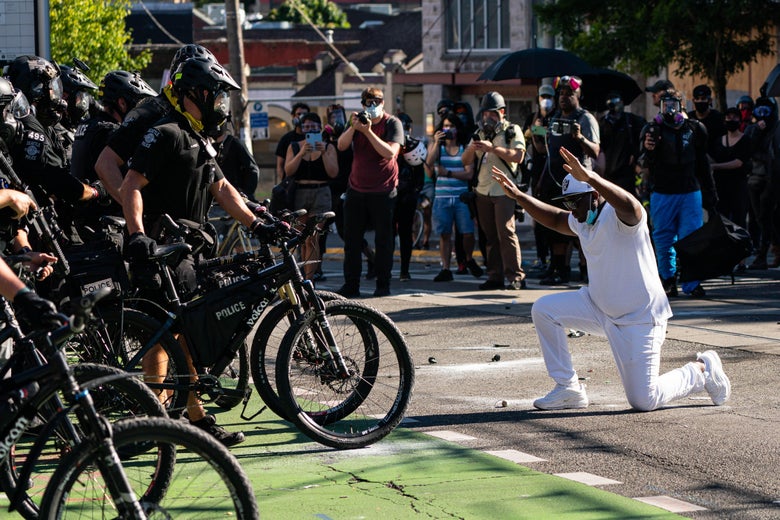 A demonstrator kneels in front of police who are standing with bikes.