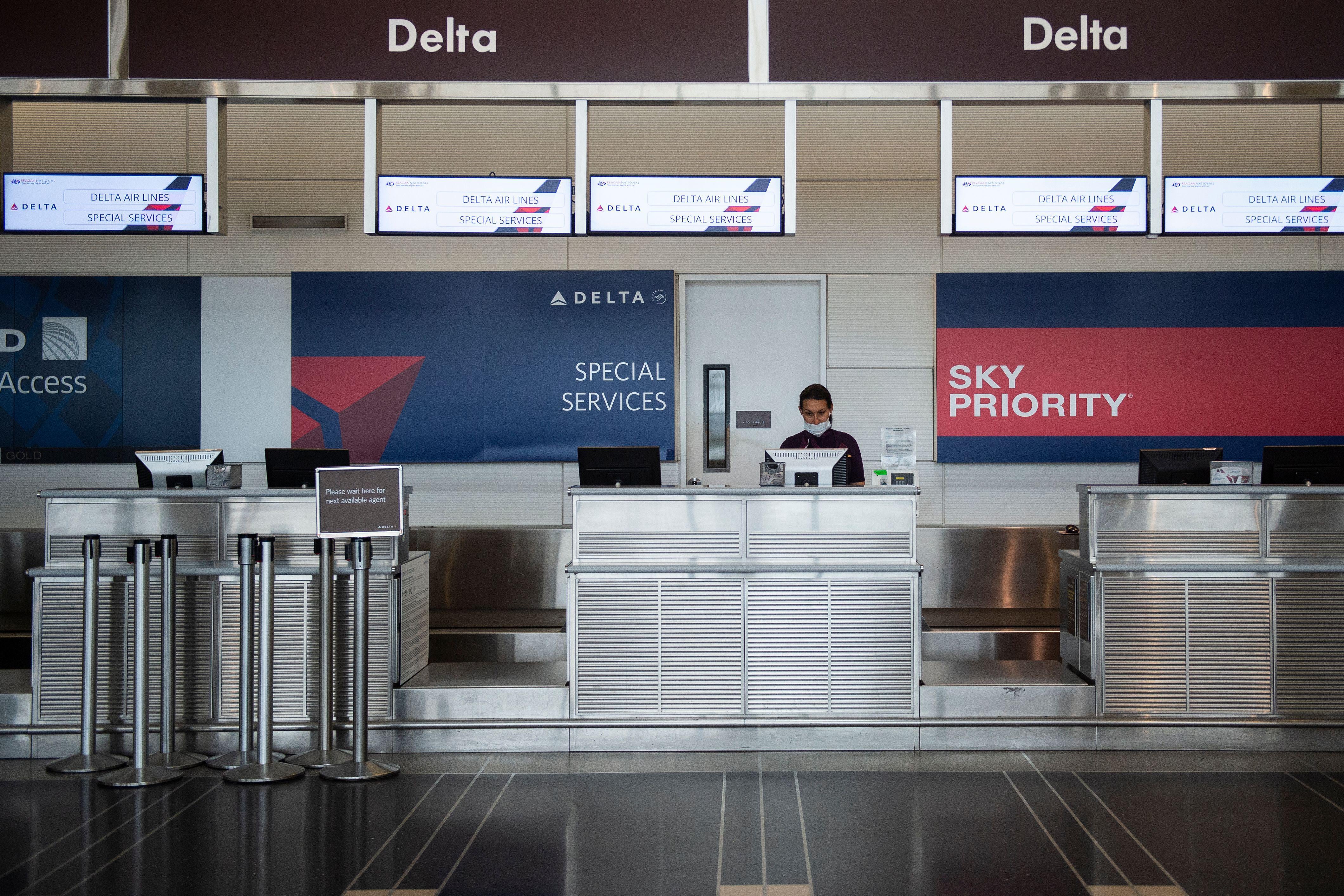 A Delta Air Lines employee waits for passengers at an empty check-in counter in Ronald Reagan Washington National Airport in Arlington, Virginia, on May 12, 2020. - The airline industry has been hit hard by the COVID-19 pandemic, with the number of people flying having decreased by more than 90 percent since the beginning of March. (Photo by ANDREW CABALLERO-REYNOLDS / AFP) (Photo by ANDREW CABALLERO-REYNOLDS/AFP via Getty Images)