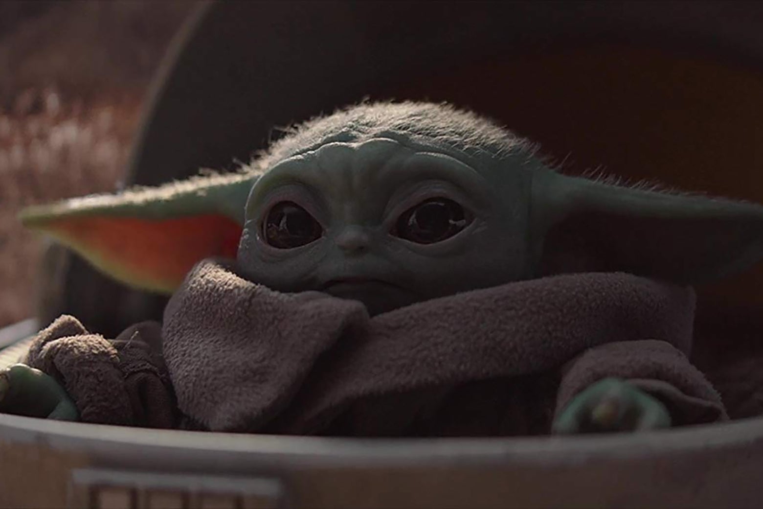 The adorable Baby Yoda creature from the Mandalorian, poking its head up from its pram.